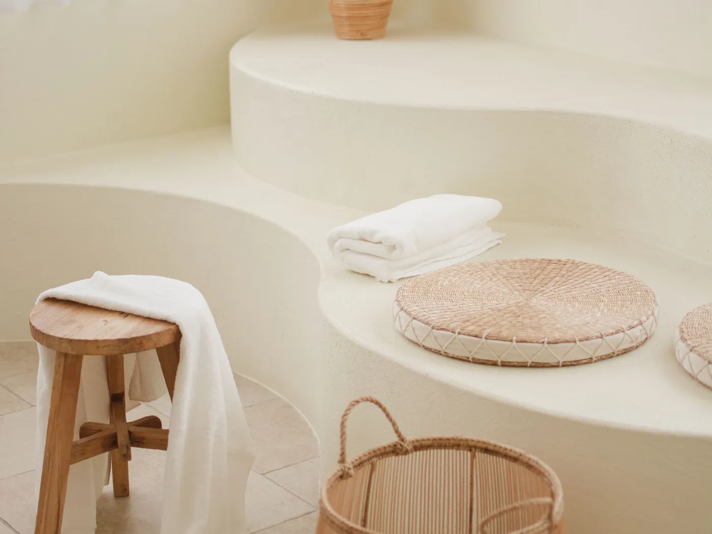 Salle de bain moderne aux lignes courbes blanches, étagères maçonnées organiques, tabouret en bois et paniers en osier.