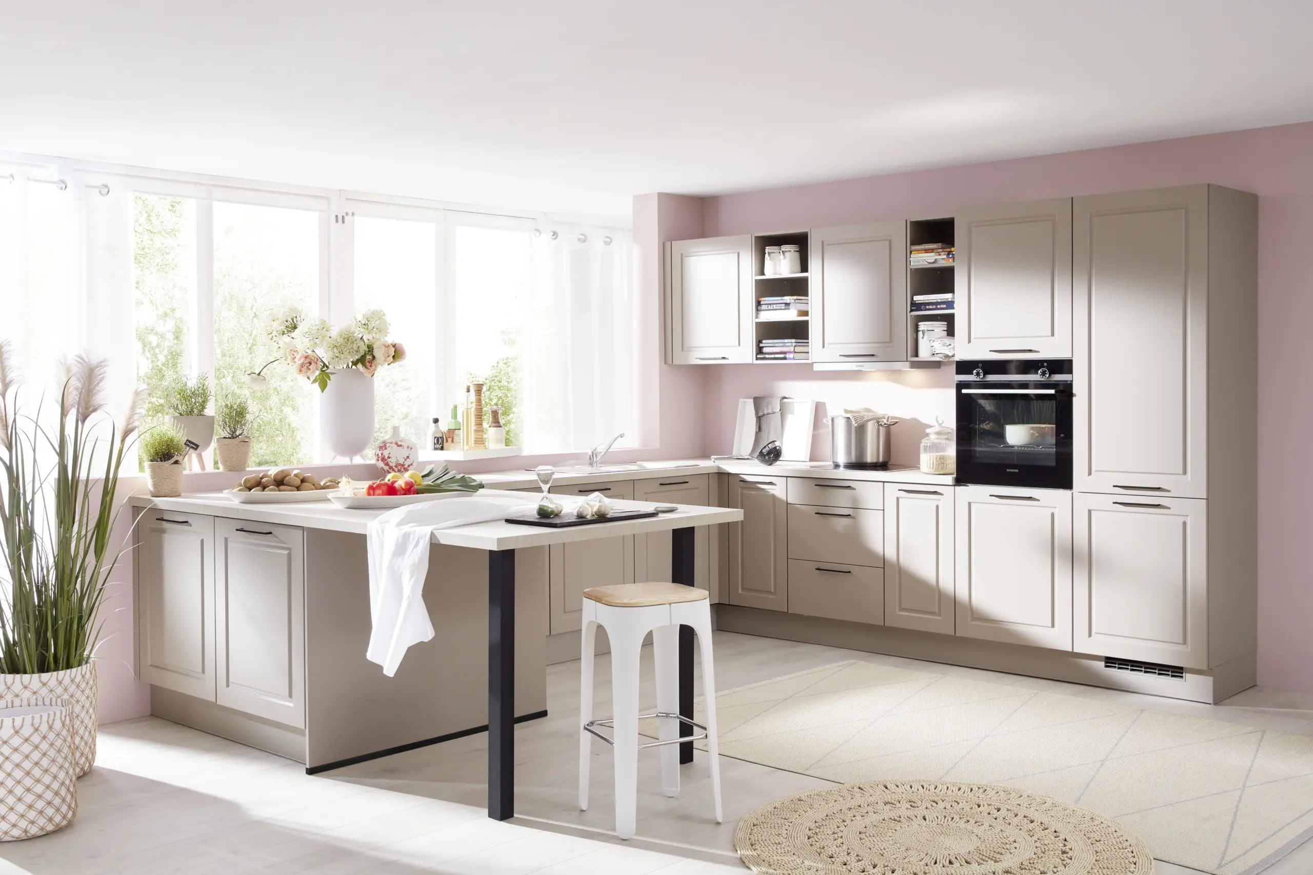 Cuisine style champêtre moderne beige avec îlot dînatoire, murs roses et grande fenêtre lumineuse.