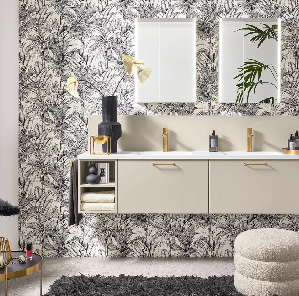 Meuble de salle de bain beige design : Double vasque élégante posée sur un meuble suspendu crème devant un papier peint aux motifs tropicaux.