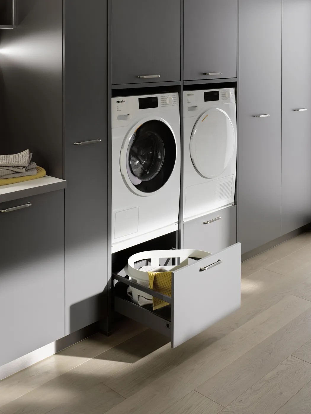 Buanderie moderne intégrée dans un placard gris avec lave-linge et sèche-linge surélevés et tiroir de rangement.