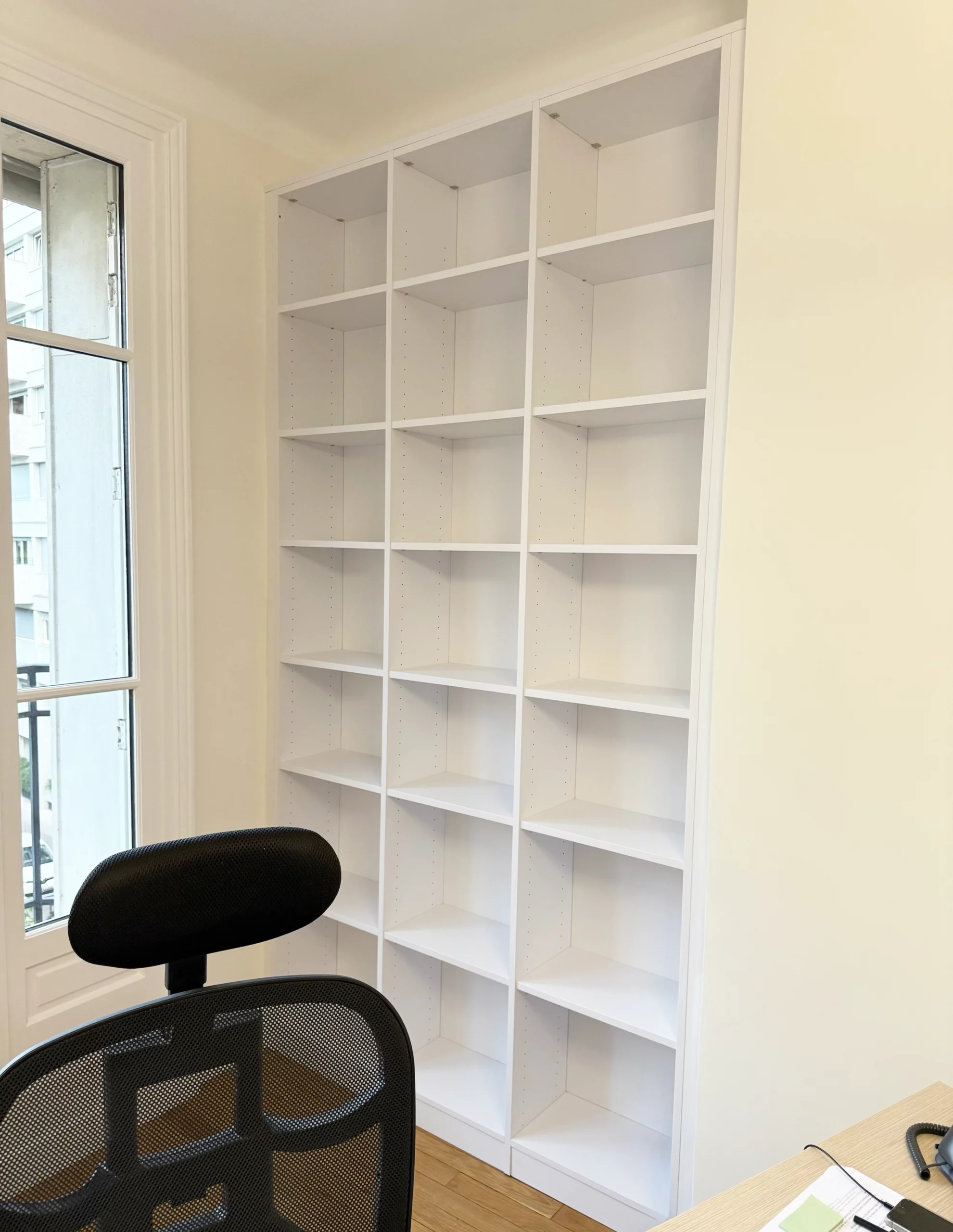 Bibliothèque blanche toute hauteur installée dans un coin bureau, offrant de multiples compartiments de rangement ouverts pour les livres et dossiers.