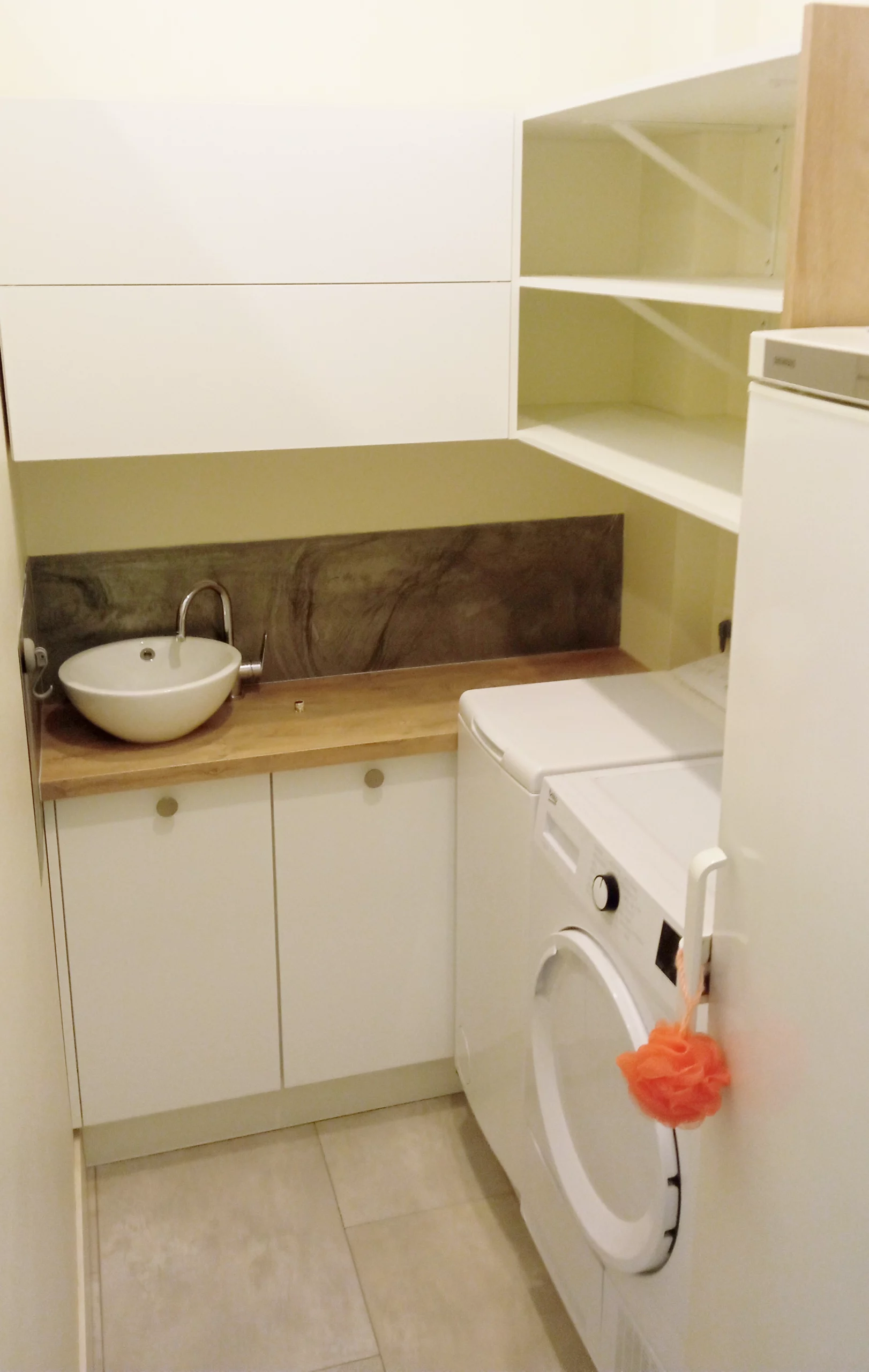 Optimisation d'un petit cellier ou buanderie avec étagères de rangement murales, lave-linge frontal et évier d'appoint sur un plan de travail en chêne.