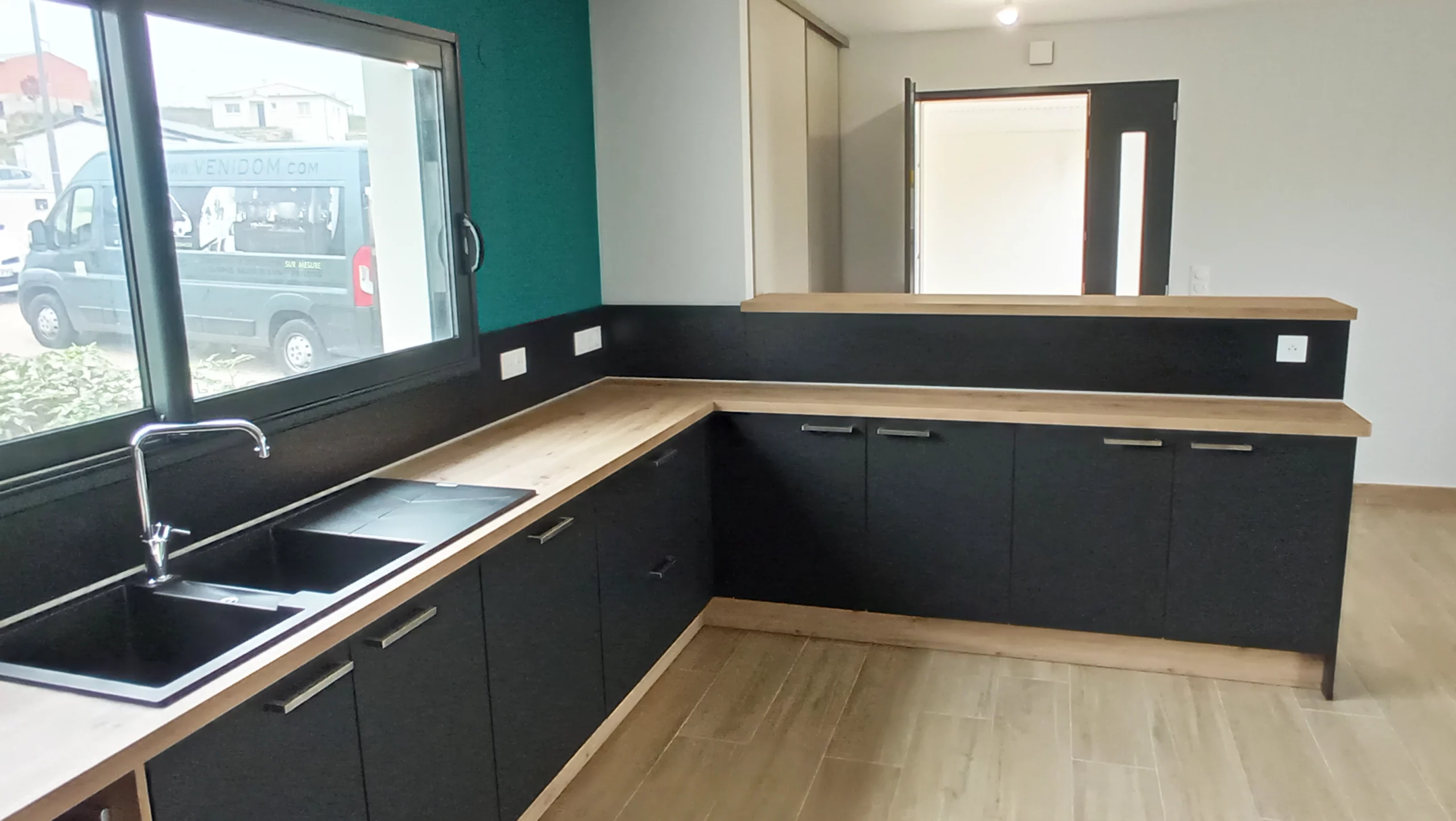 Détail plan de travail bois et évier noir : Zoom sur l'angle d'une cuisine en bois et noir mat avec évier encastré sous une fenêtre, illustrant la qualité des finitions et l'optimisation de l'espace.