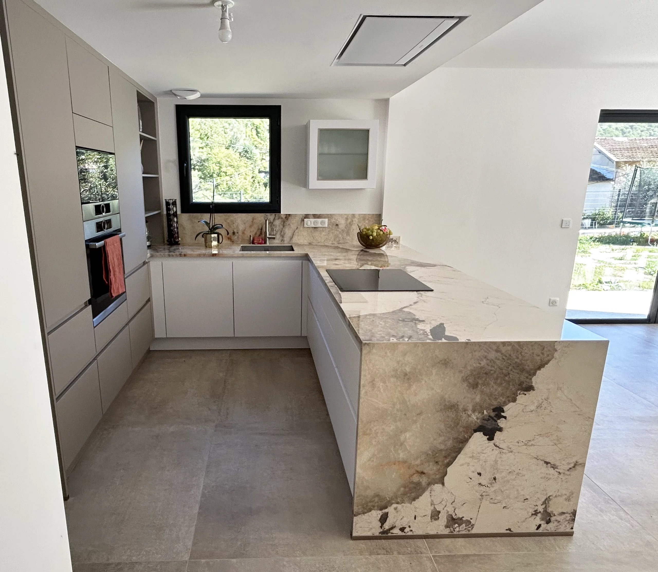 Vue lumineuse d'une cuisine ouverte avec îlot central sculptural, électroménager moderne et grandes baies vitrées offrant une vue dégagée sur l'extérieur.