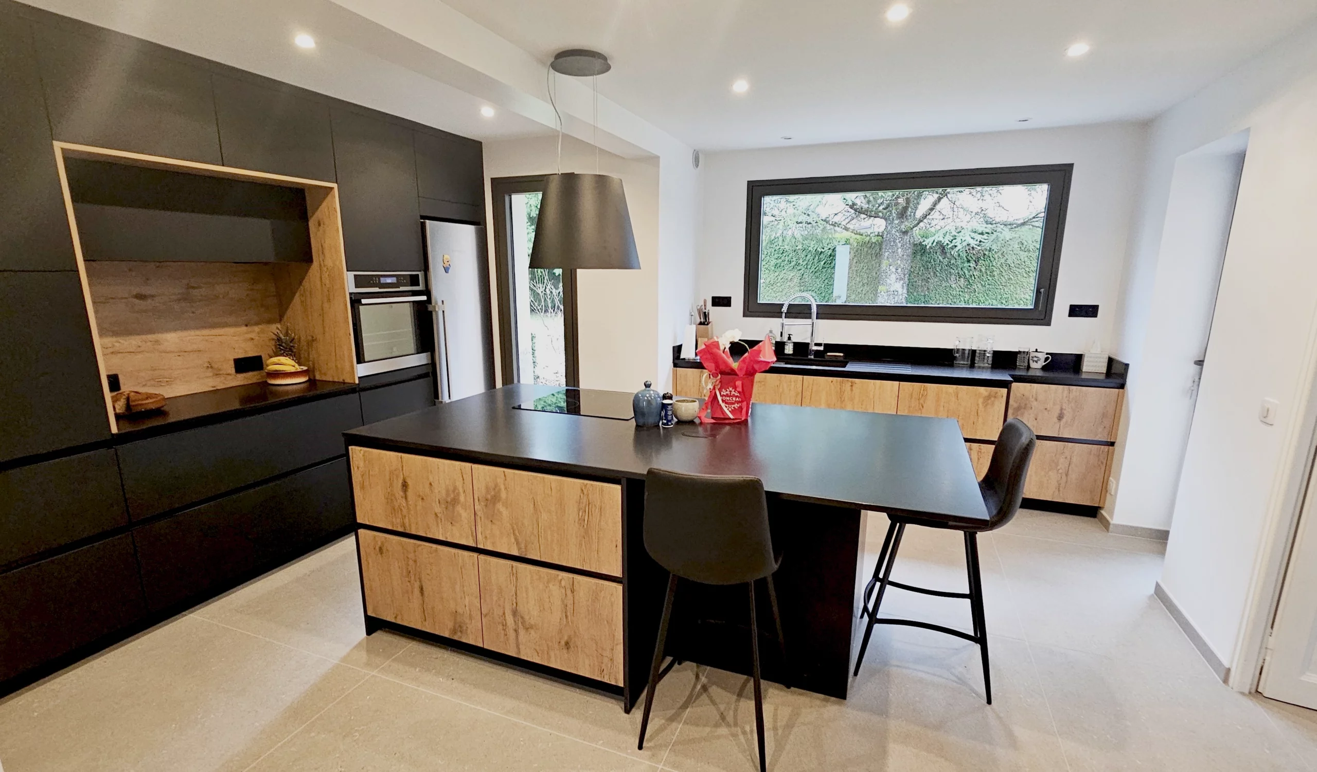 Cuisine moderne avec îlot noir et table bois : Réalisation associant un îlot central sombre, une table à manger en bois naturel et des chaises vert canard dans un espace ouvert.
