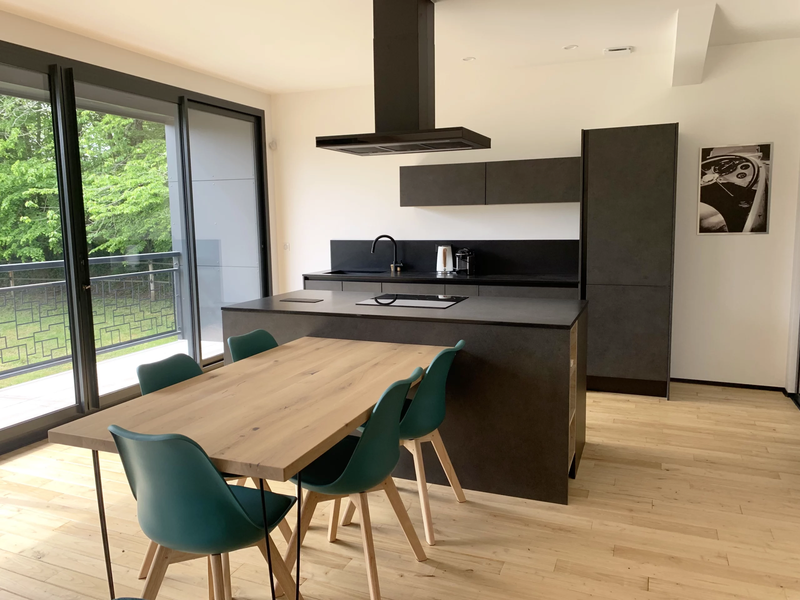 Cuisine ouverte avec table en bois : Réalisation moderne associant un îlot central noir mat et une grande table à manger en chêne naturel dans un espace lumineux.