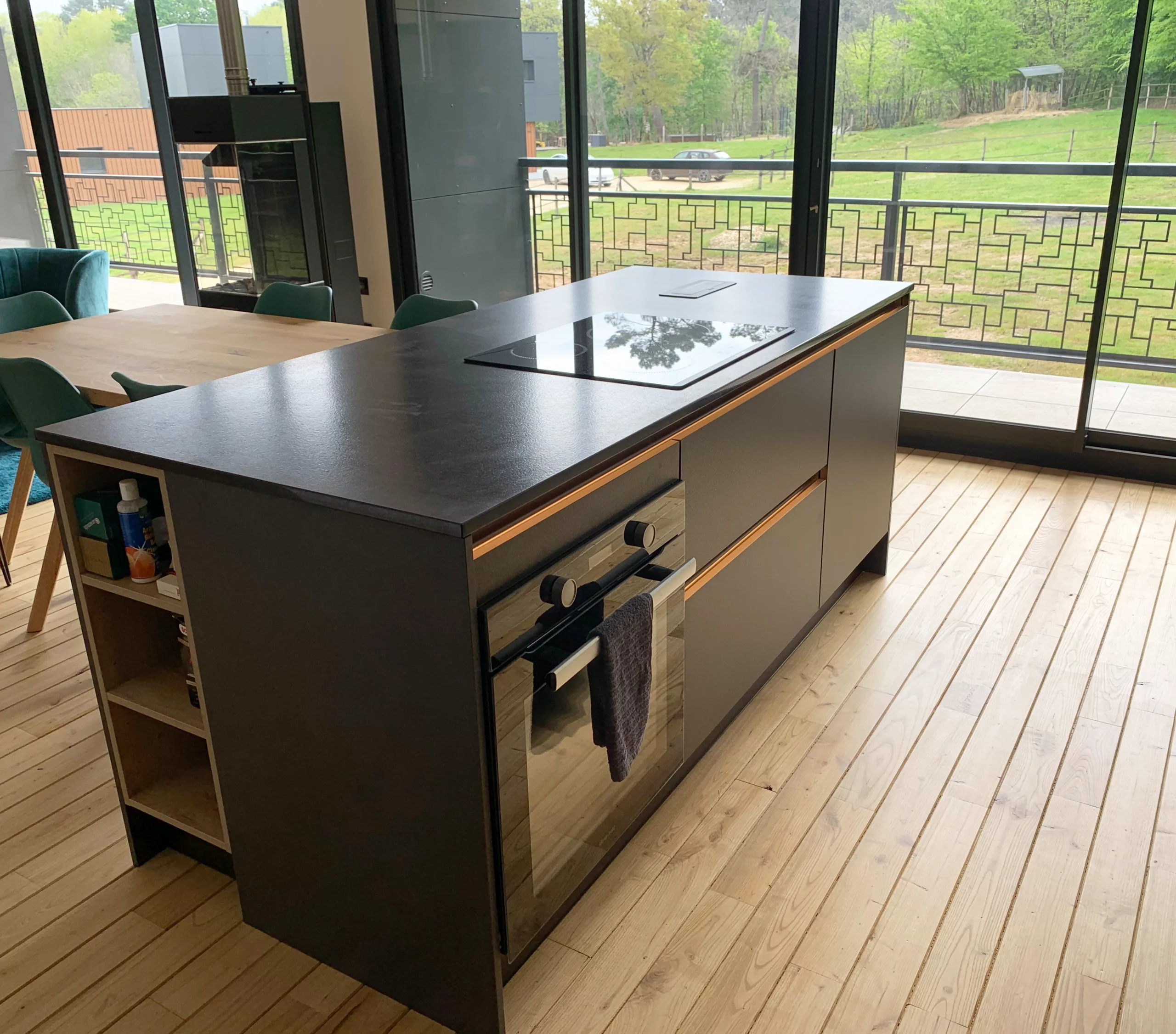 Zoom îlot central noir et bois : Vue détaillée d'un îlot de cuisine avec plaque de cuisson intégrée, placards sombres et finitions latérales en bois clair.