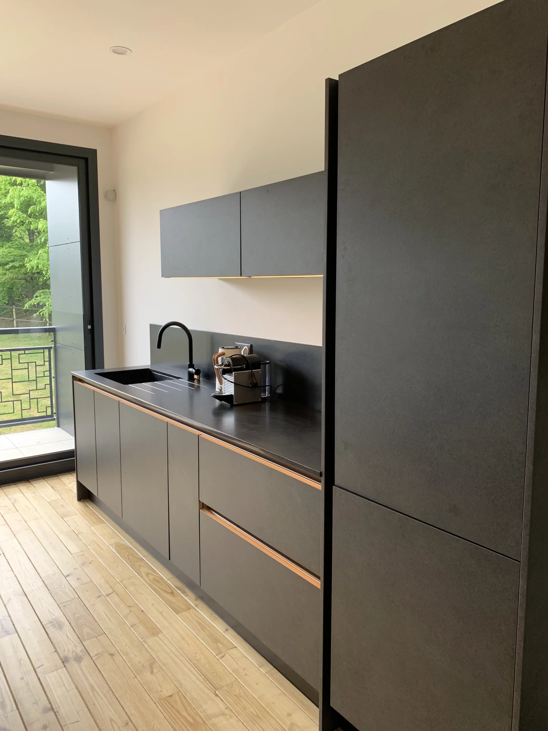 Cuisine linéaire minimaliste : Aménagement de cuisine contre un mur avec façades noires sans poignées et plan de travail en bois chaleureux.