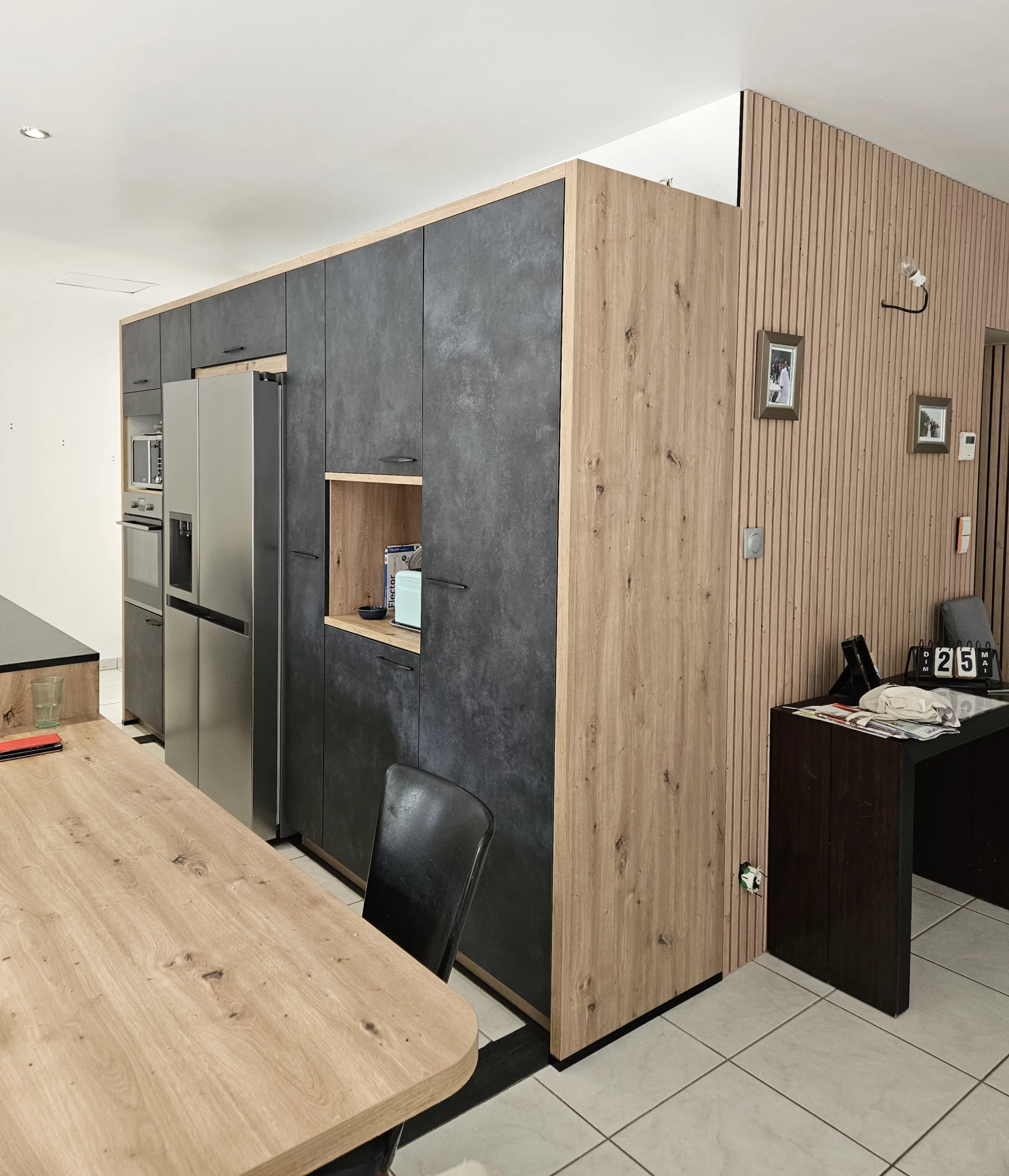Aménagement de cuisine bois et anthracite avec coin bureau : Vue latérale d'un grand ensemble de cuisine sur mesure intégrant l'électroménager et se prolongeant par un petit espace bureau fonctionnel.