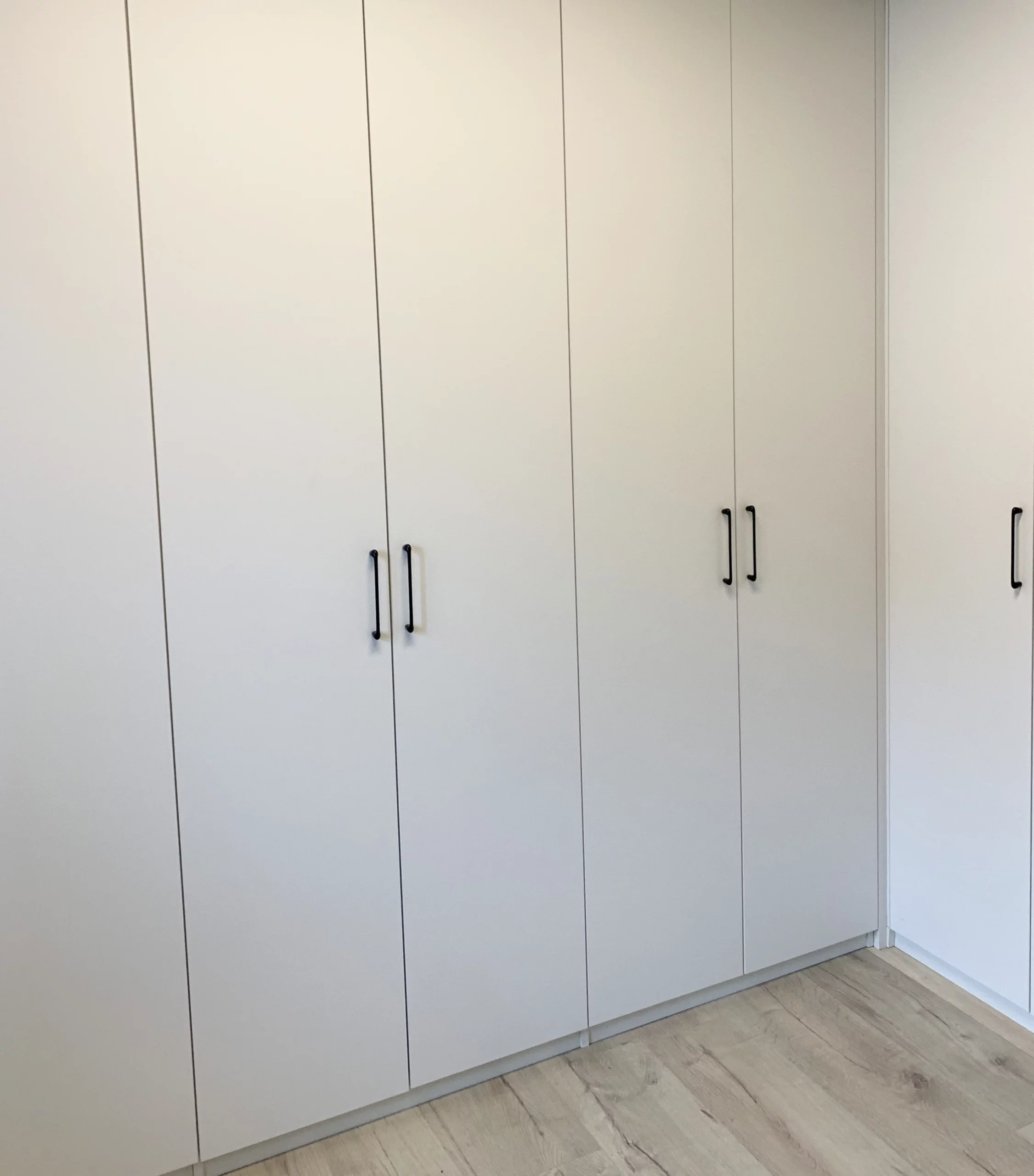 Vue de face d'un grand placard de rangement aux façades blanches épurées et poignées verticales fines, s'intégrant parfaitement dans une pièce moderne.
