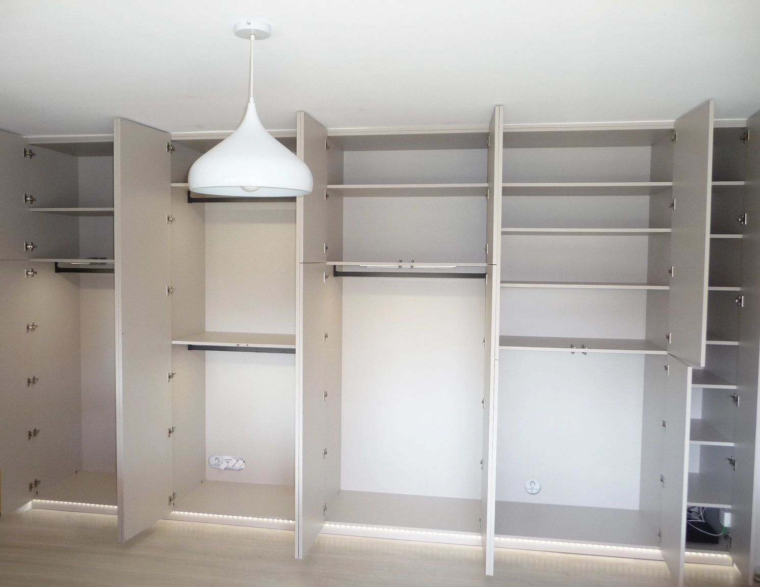 Vue de l'intérieur d'un grand dressing sur mesure aux tons beige sable, comprenant de nombreuses étagères modulables, des penderies éclairées par LED et un éclairage d'ambiance au sol.