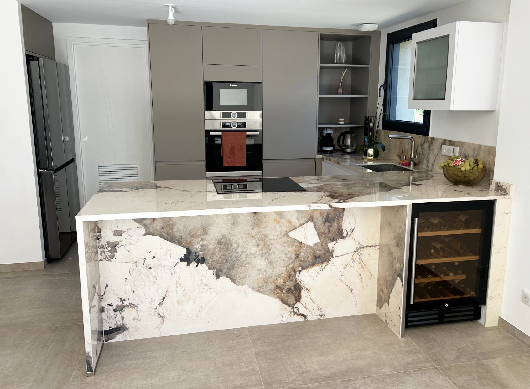 Aménagement de cuisine haut de gamme montrant l'îlot central massif en quartz veiné, un plan de travail en U et des colonnes de rangement toute hauteur.