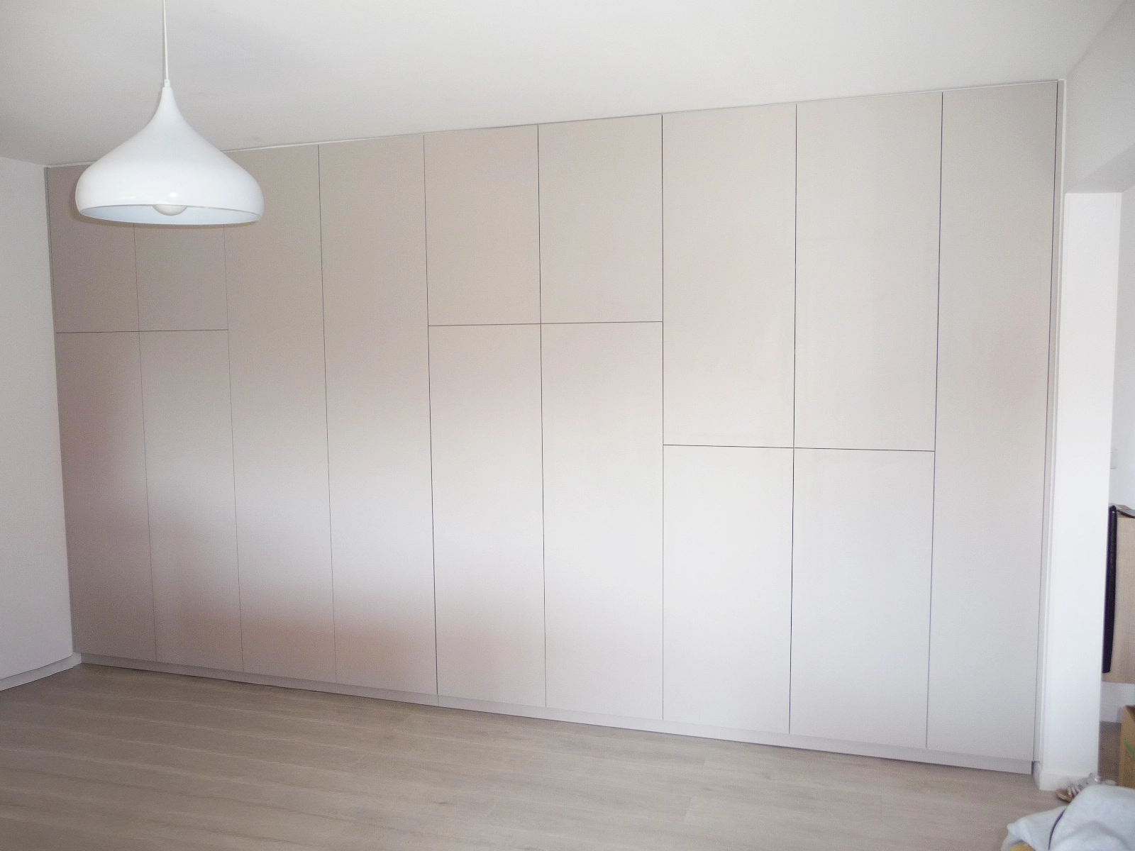 Grand dressing mural toute hauteur au design minimaliste avec des façades lisses sans poignées apparentes pour un effet discret et élégant.