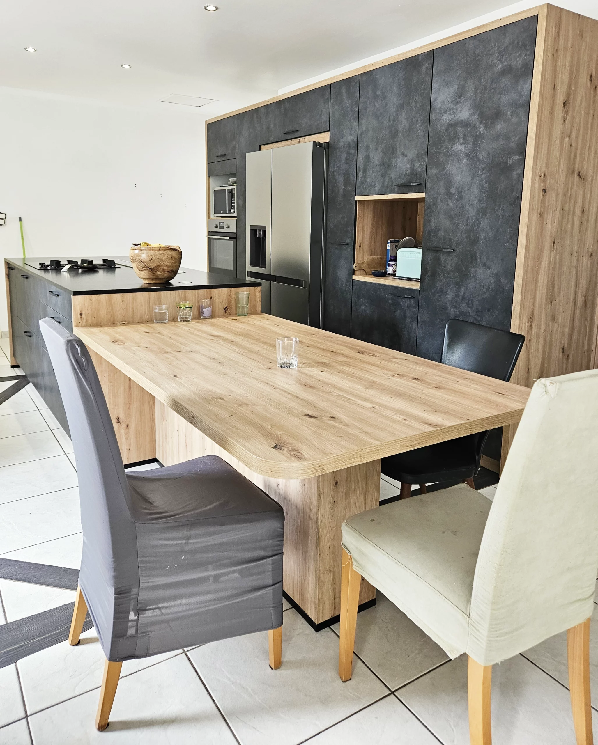 Espace repas convivial avec table en bois massif : Détail d'une cuisine ouverte montrant une grande table de repas en bois clair attenante à l'îlot, entourée de chaises design pour une ambiance chaleureuse.