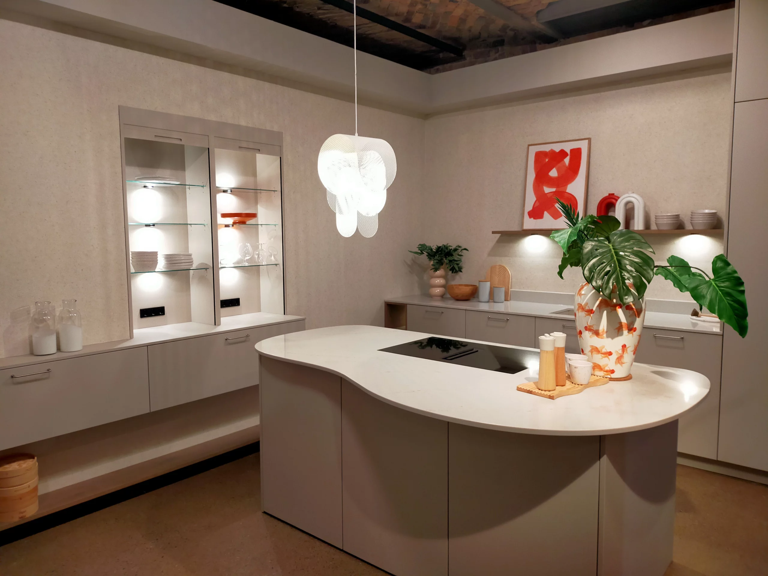 Cuisine moderne beige avec îlot central aux lignes courbes, plan de travail blanc et vitrines lumineuses.