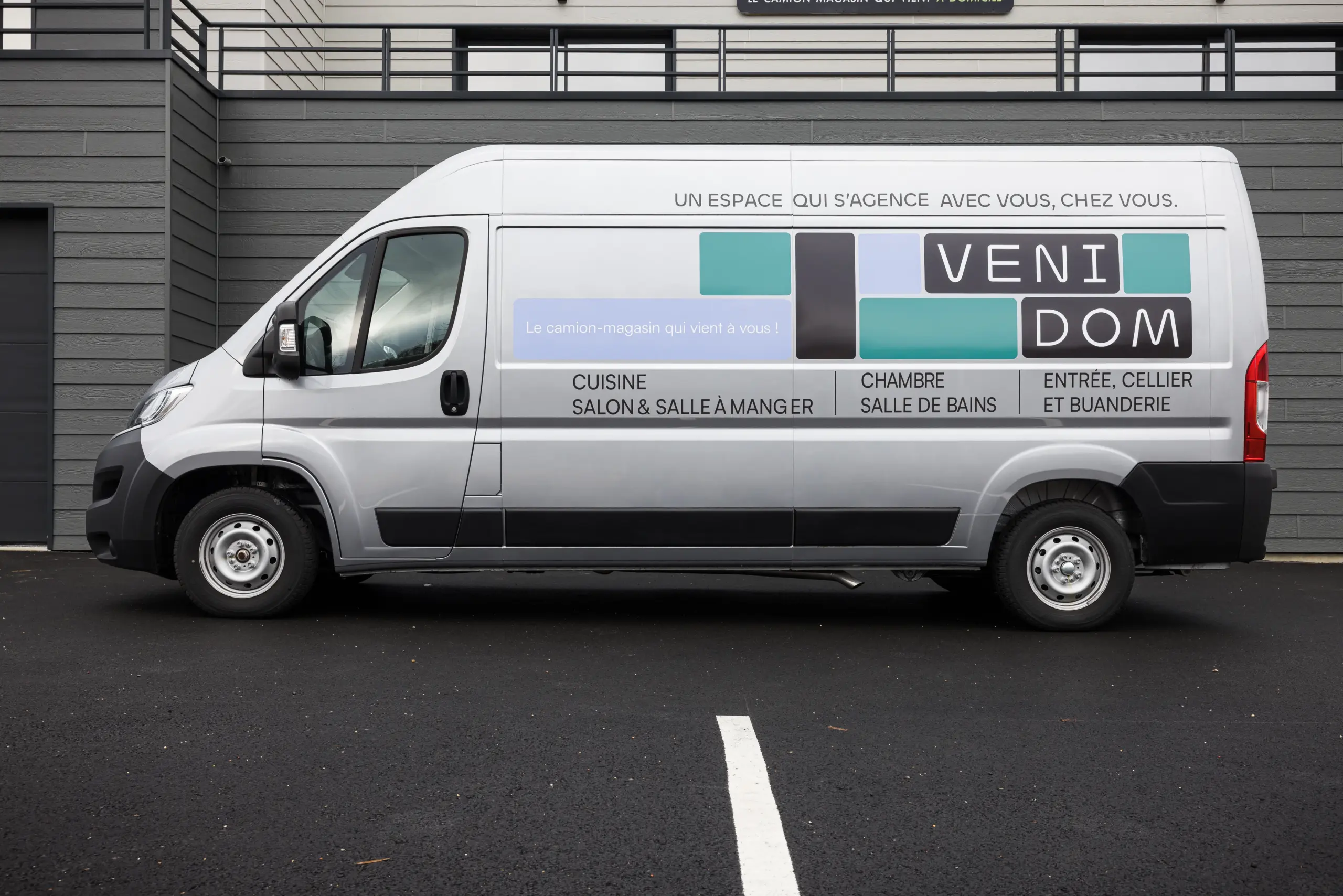 Camion-magasin Venidom de profil : Showroom mobile gris stationné présentant les services de conception de cuisine, salle de bain, chambre et dressing à domicile.