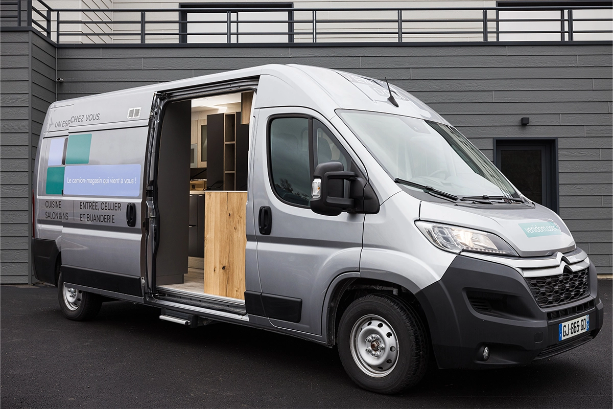 Camion-magasin Venidom, showroom mobile de cuisines, salles de bain et dressings devant un bâtiment moderne.