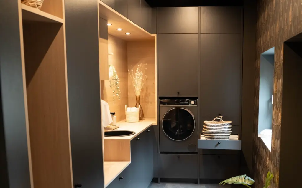 Buanderie moderne anthracite avec lave-linge encastré, tablette coulissante et niche en bois éclairée.