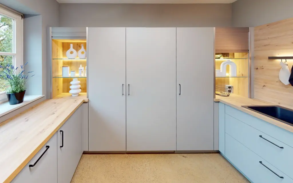 Espace hybride buanderie et cellier avec placards gris, vitrines rétroéclairées et plan de travail en bois.