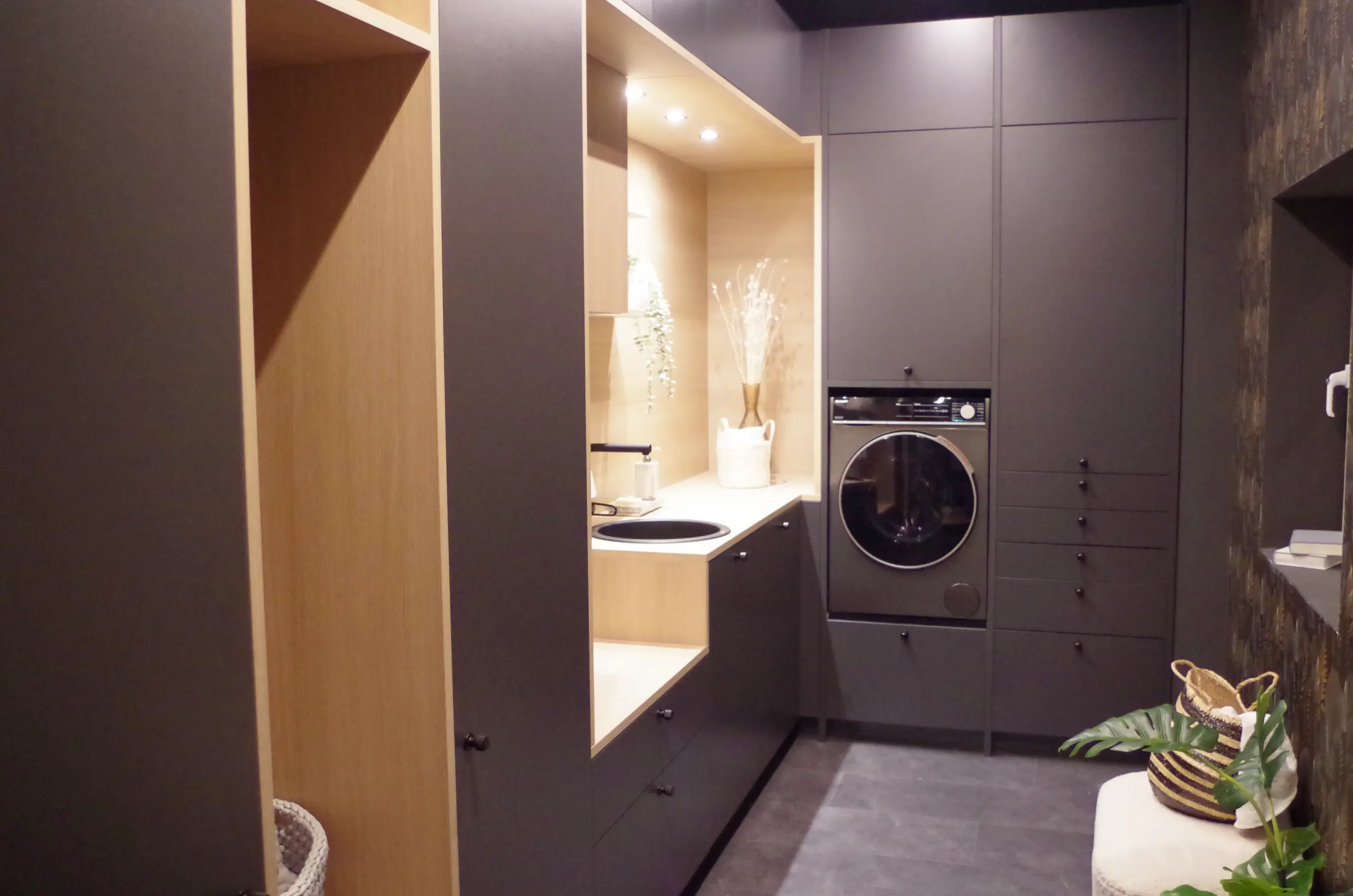 Buanderie optimisée sombre : Aménagement sur mesure pour machine à laver et rangements dans les tons gris anthracite et bois clair.