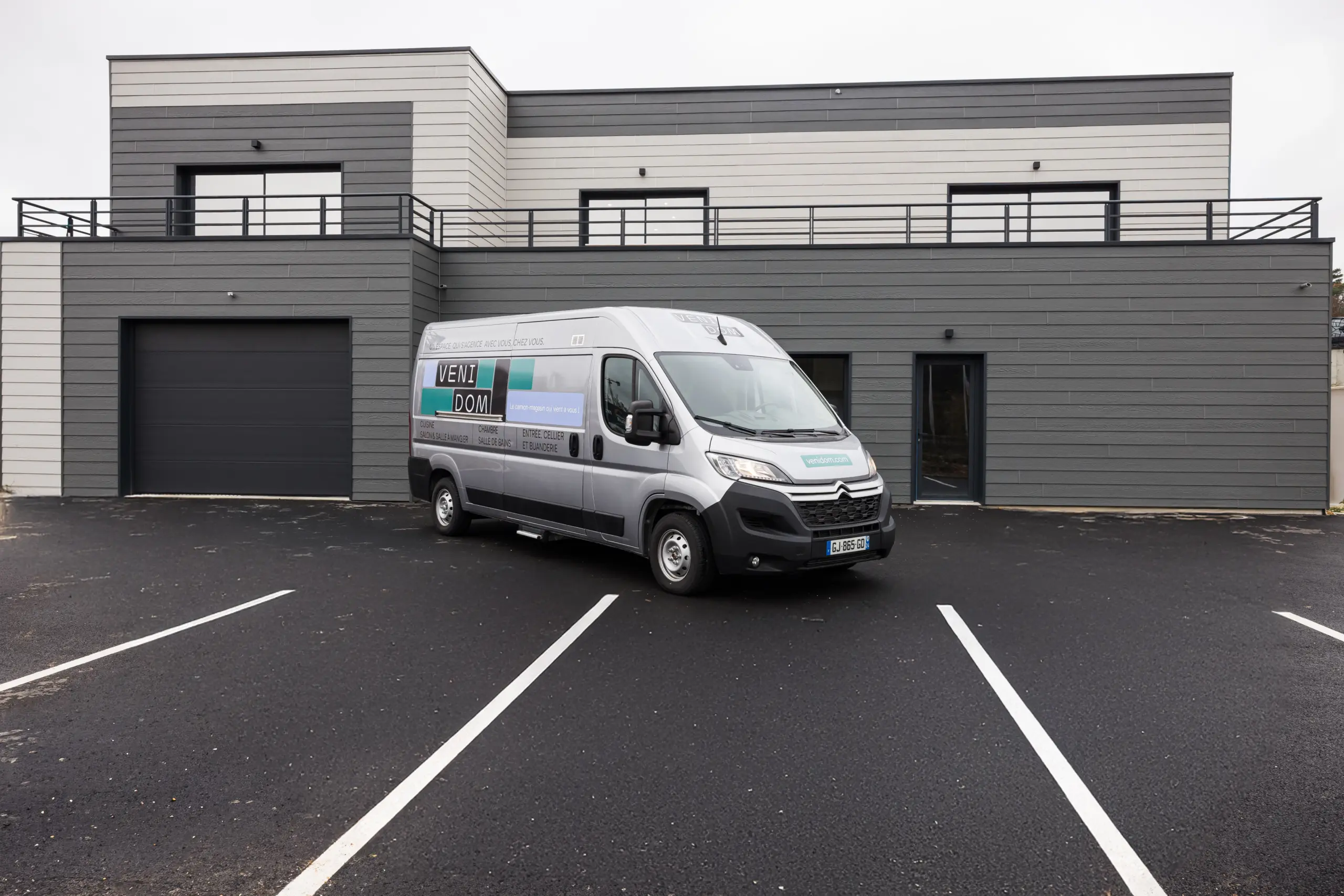Camion-magasin Venidom, showroom mobile pour projets de cuisine et aménagement intérieur, stationné devant un bâtiment moderne.
