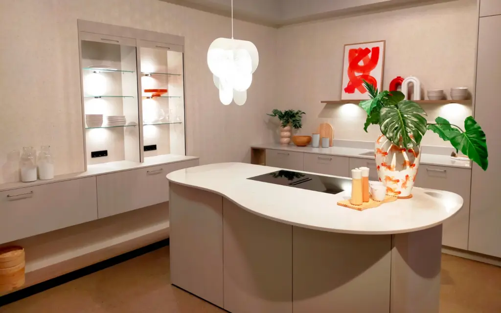 Cuisine moderne beige avec îlot central courbe, plan de travail blanc et vitrines lumineuses encastrées.