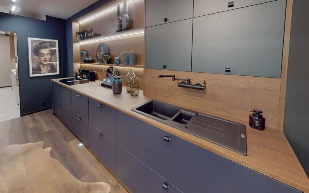 Cuisine linéaire bleu encre et bois avec évier noir intégré, étagères rétroéclairées et décoration murale.