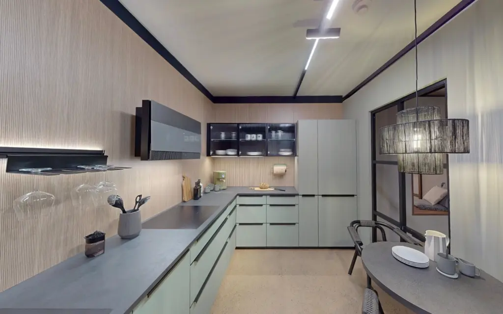 Cuisine moderne vert sauge et bois avec plan de travail gris, crédence en bois strié et coin repas intégré.