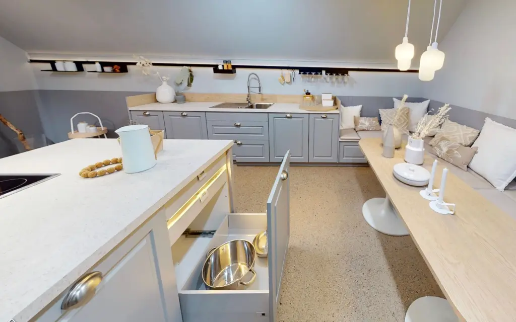 Cuisine grise moderne sous pente avec îlot central, tiroirs éclairés et coin repas banquette intégré.