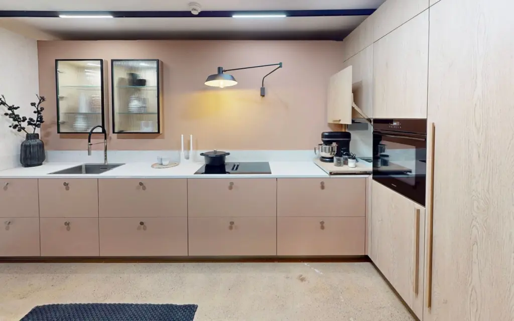 Petite cuisine moderne rose poudré et bois clair avec vitrines suspendues et électroménager encastré.