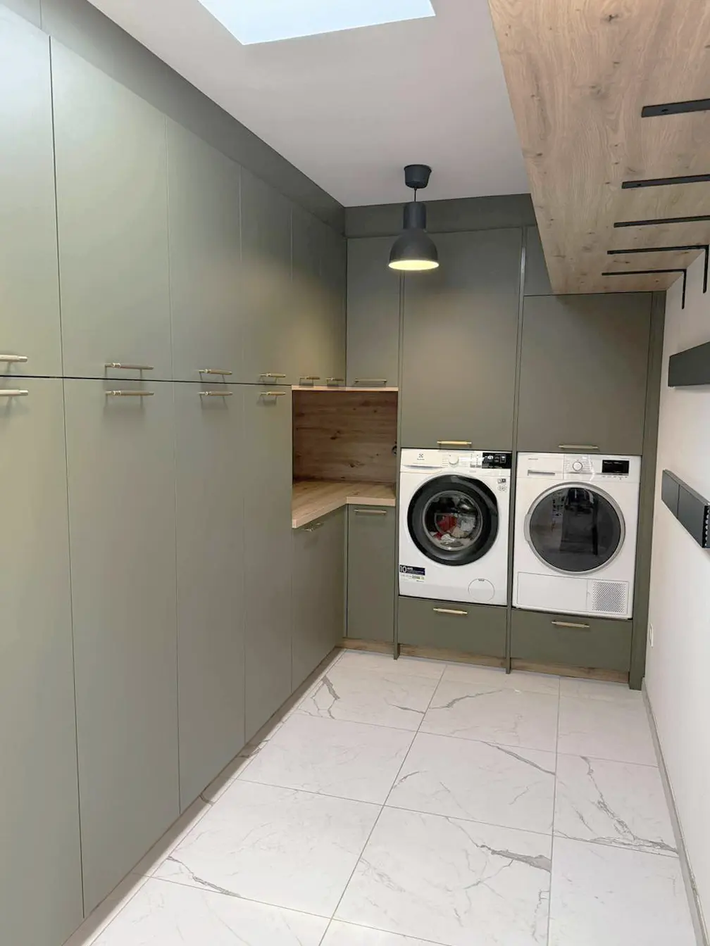 Aménagement de buanderie ergonomique avec lave-linge et sèche-linge surélevés à hauteur d'homme, entourés de colonnes de rangement verticaux vert olive.