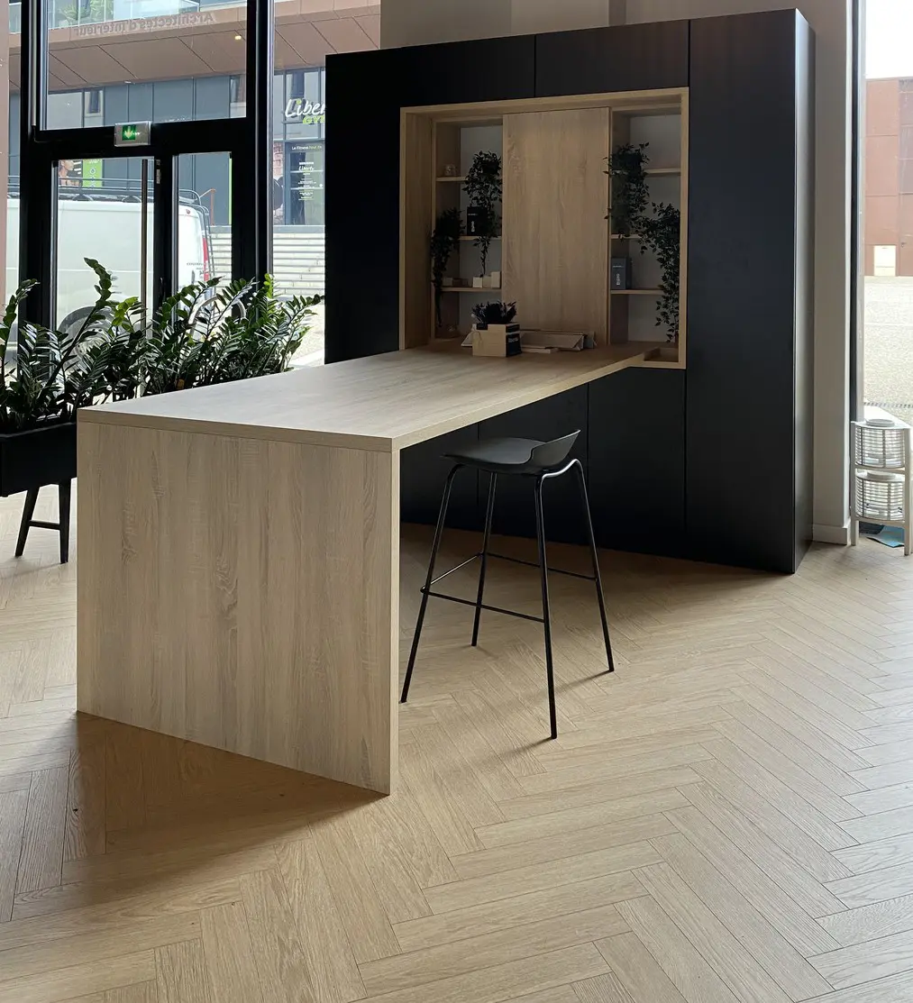 Bureau sur-mesure en bois chaleureux intégré dans un ensemble de rangements noirs mats avec niches ouvertes accueillant des plantes vertes, conçu par Wilfrid Corneau pour créer un espace de travail ressourçant.