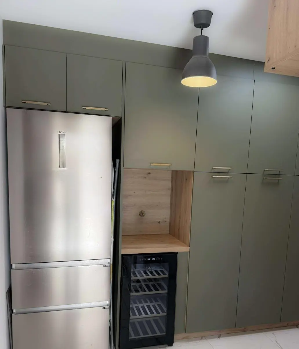 Cellier optimisé par Maximilien Lust (Venidom Grand Littoral) intégrant un réfrigérateur américain et une cave à vin dans un ensemble de meubles sur mesure vert sauge et bois.