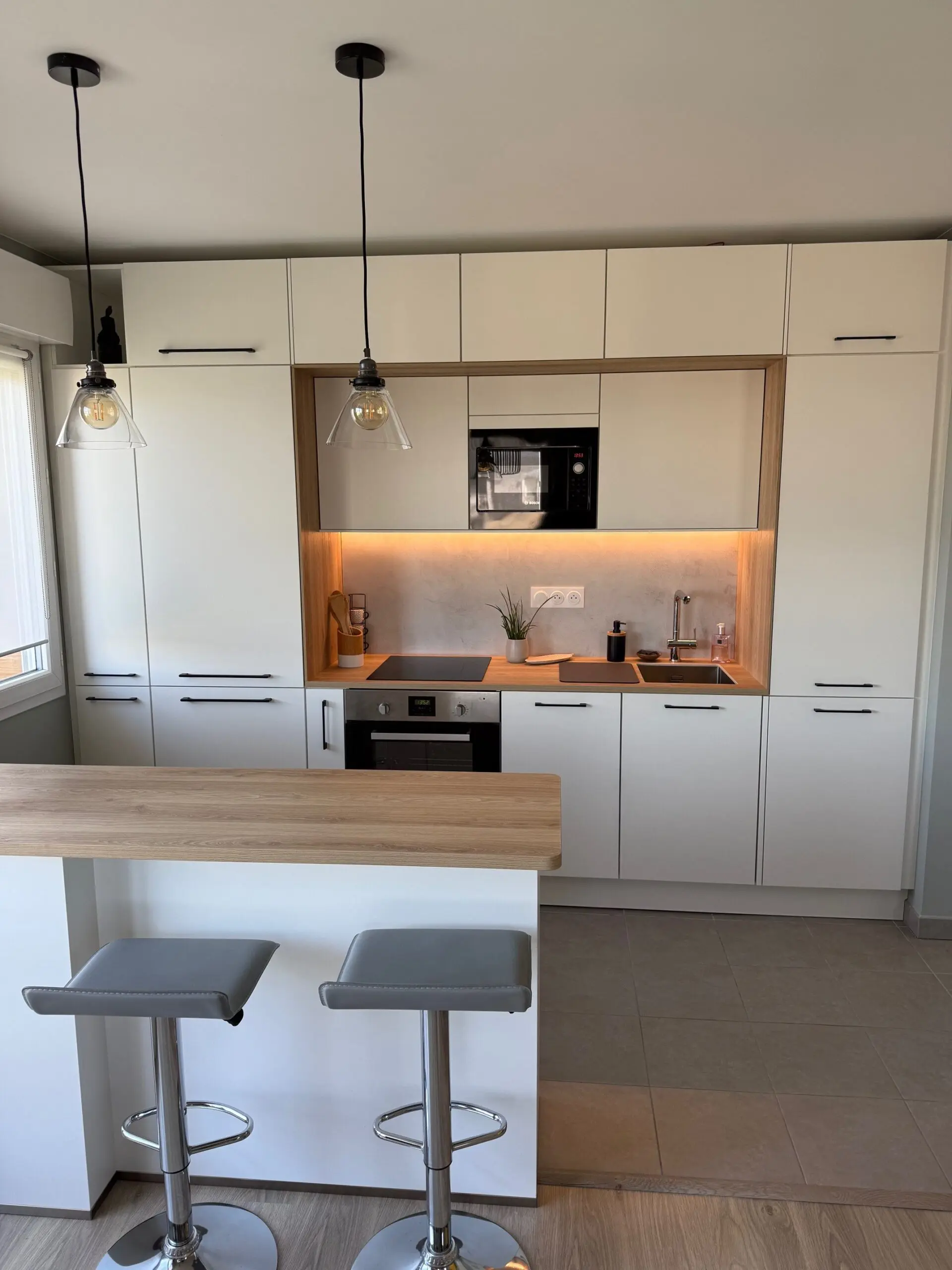 Îlot de cuisine fonctionnel avec façades blanches et plan de travail en chêne, prolongeant l'espace de préparation vers le salon pour plus de convivialité.