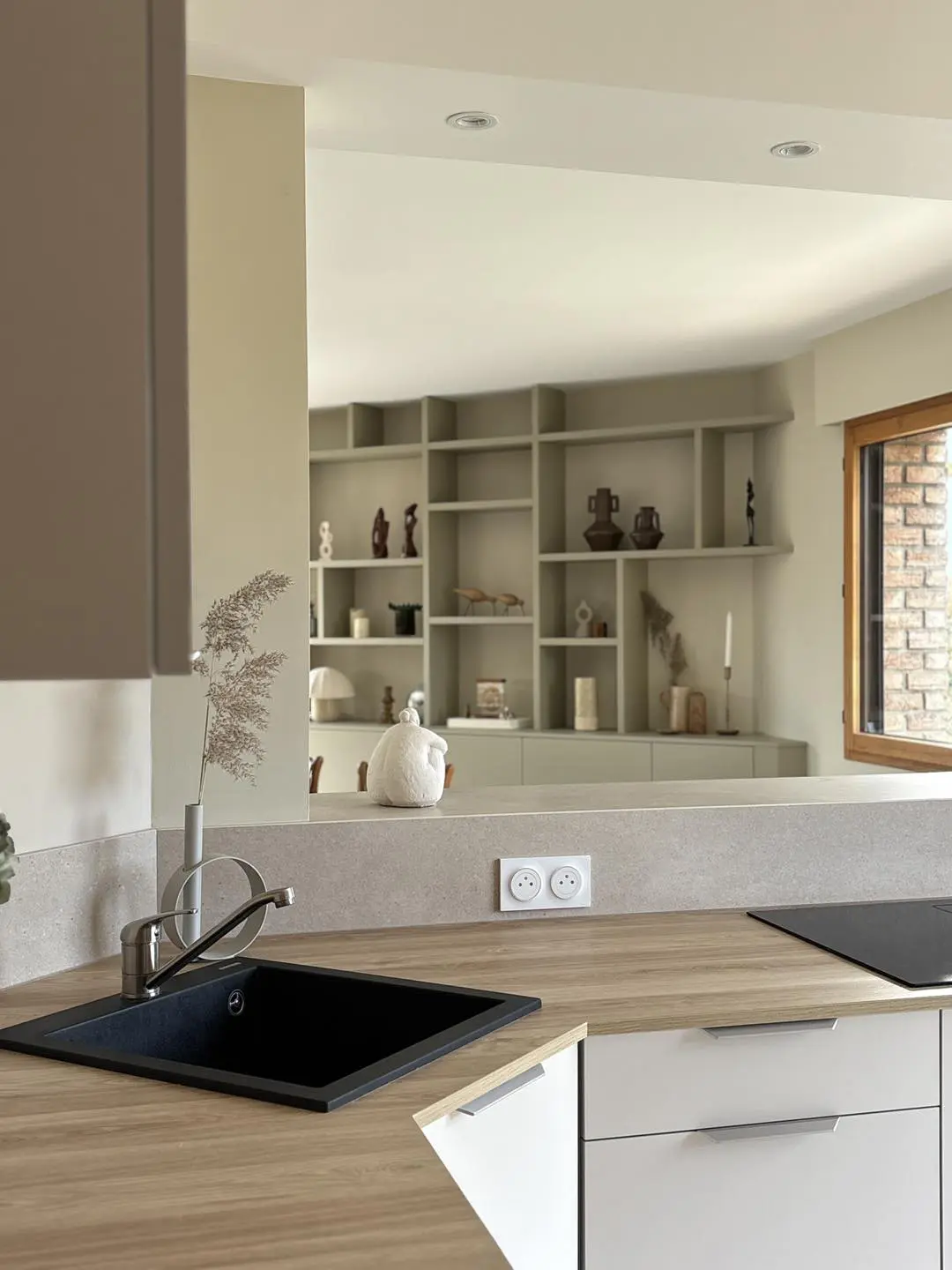 Zone de lavage optimisée avec évier noir et plan de travail bois, baignée de lumière naturelle grâce à l'ouverture de l'espace sur le reste de la maison.