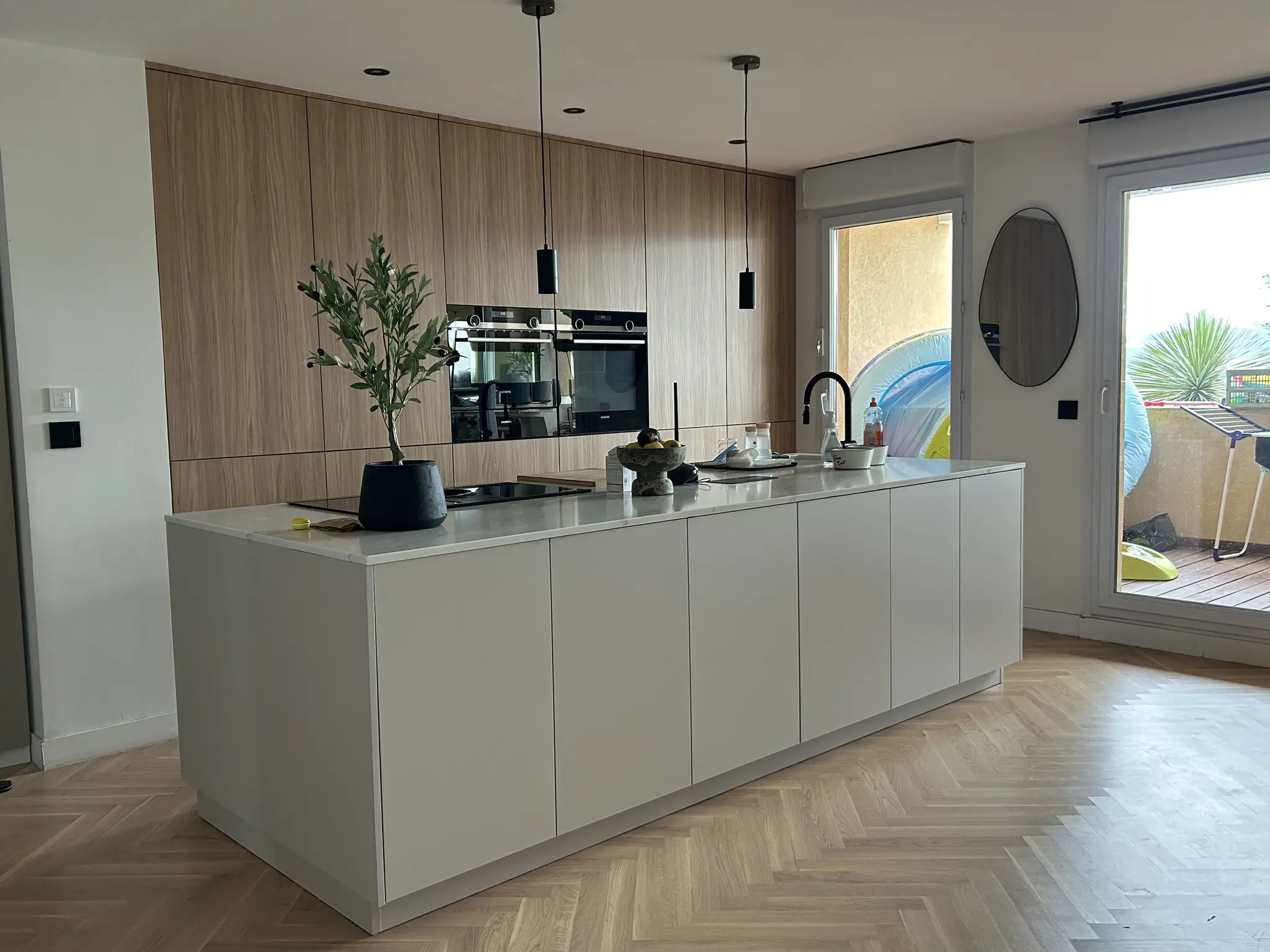 Transformation esthétique d'une cuisine existante conservant son implantation optimisée avec un îlot central généreux et des finitions en bois naturel baignées de lumière.