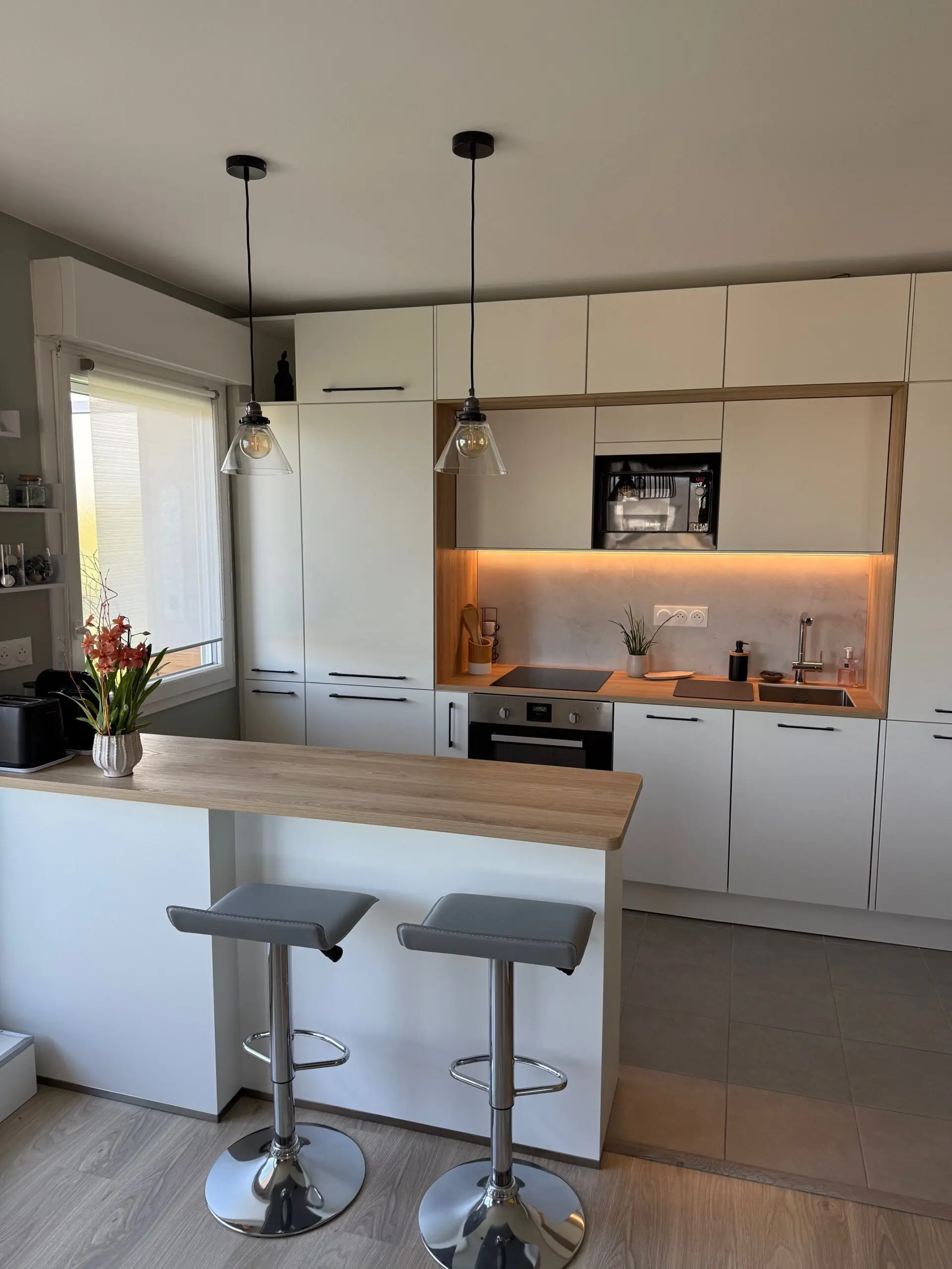 Îlot de cuisine fonctionnel avec façades blanches et plan de travail en chêne, prolongeant l'espace de préparation vers le salon pour plus de convivialité.