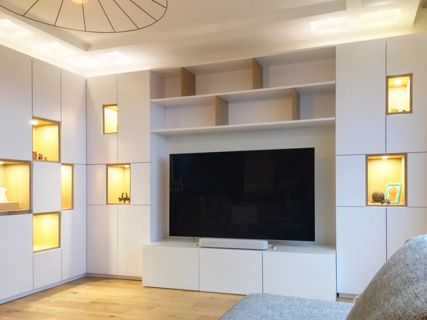 Composition murale sur-mesure en blanc mat avec meuble TV intégré et niches décoratives rétroéclairées, conçue pour optimiser l'espace vertical par Wilfrid Corneau.