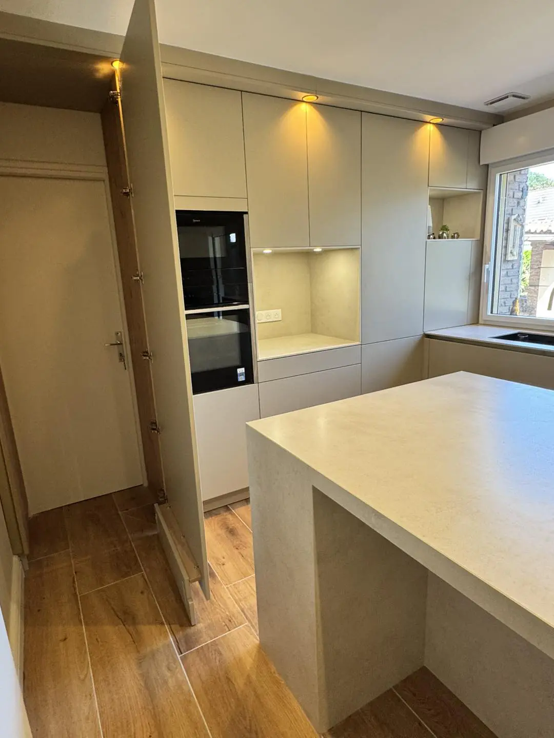 Porte invisible intégrée sans poignées dans un mur de colonnes de cuisine, offrant un accès discret à l'arrière-cuisine tout en préservant l'esthétique épurée.