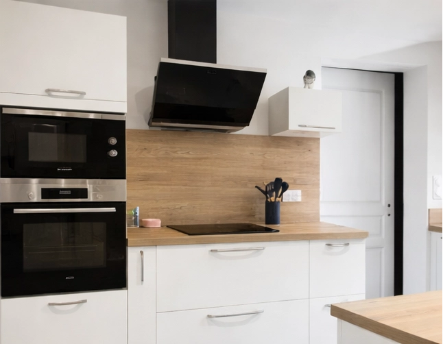 Zoom sur le pôle cuisson d'une cuisine contemporaine. Il comprend une plaque à induction noire sur un plan de travail en bois, surmontée d'une hotte aspirante noire inclinée. À gauche, une colonne intègre un four et un micro-ondes encastrés. La crédence assortie au plan de travail apporte une touche chaleureuse.