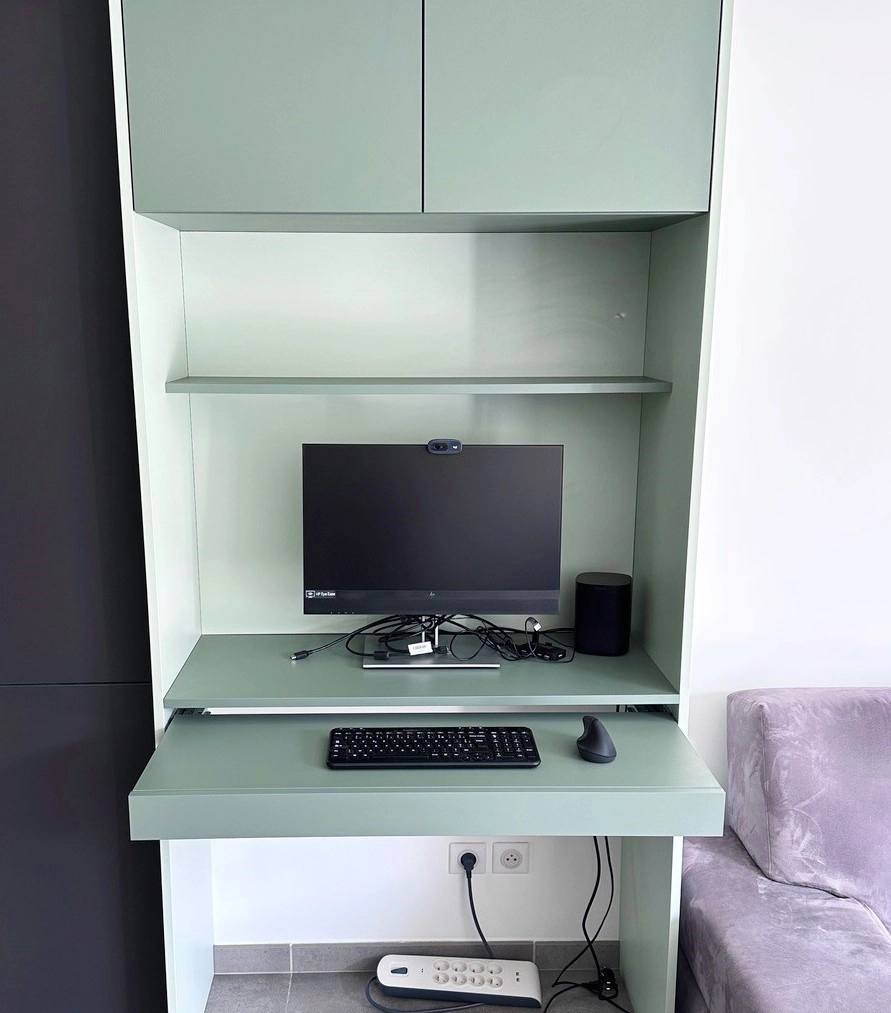 Gros plan d'un coin bureau sur mesure de couleur vert sauge, doté de rangements en hauteur, d'une étagère intermédiaire et d'un plateau de travail équipé d'un écran et d'un clavier.