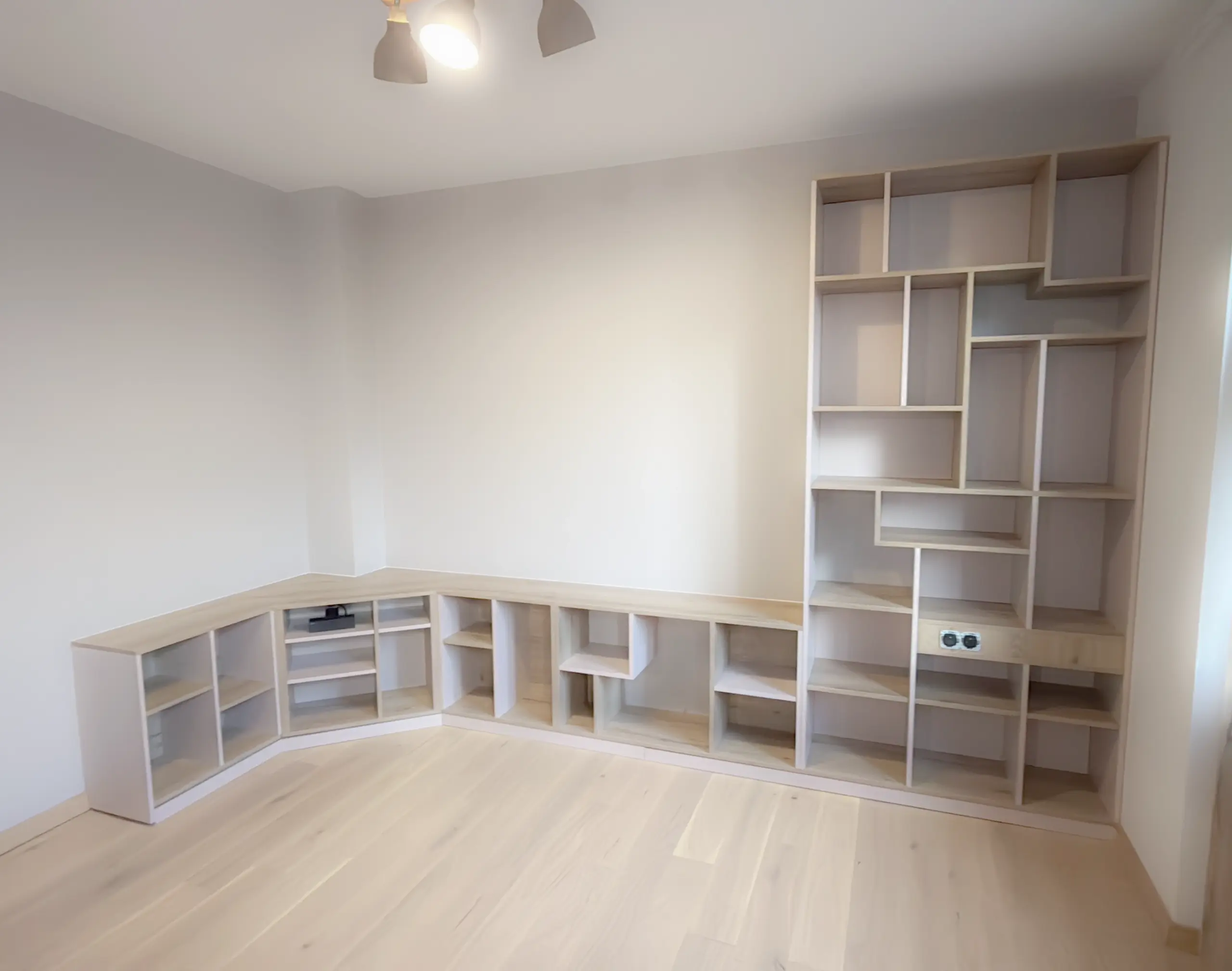 Aménagement de salon avec bibliothèque d’angle en bois et rangements modulables pour livres, jeux et objets du quotidien