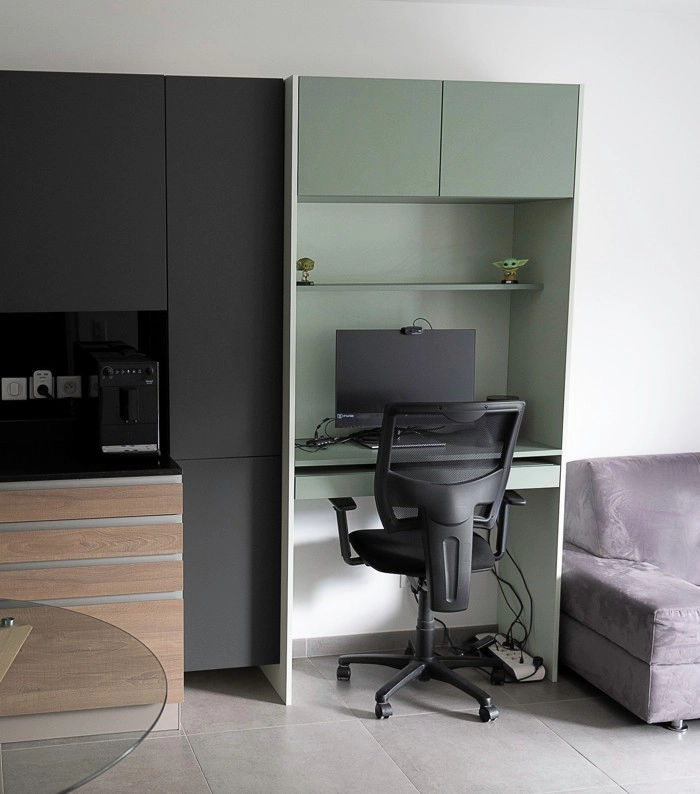 Aménagement architectural d'un bureau vert sauge niché à côté d'un meuble de cuisine noir mat, illustrant une transition fluide et esthétique dans une pièce de vie ouverte.