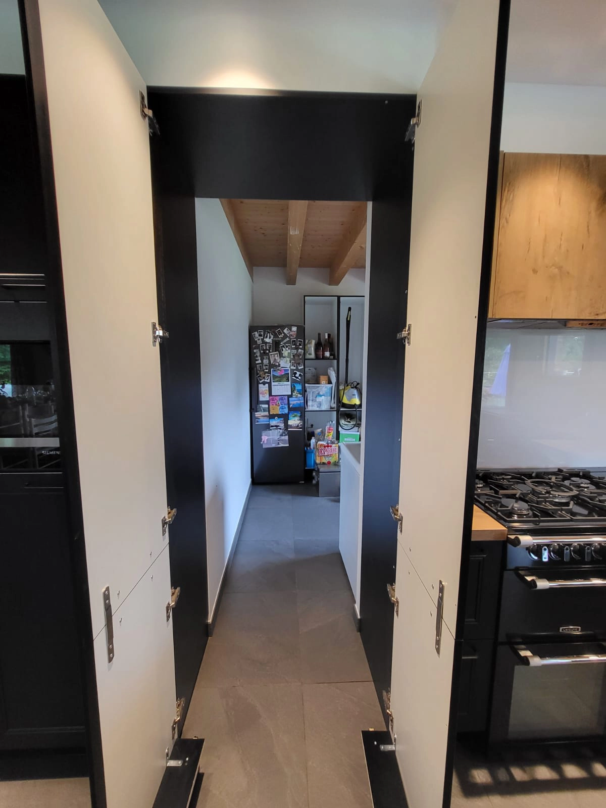 Porte de cuisine ouverte révélant une pièce cachée servant de cellier et d'arrière-cuisine pour maximiser le stockage sans encombrer l'espace visuel.