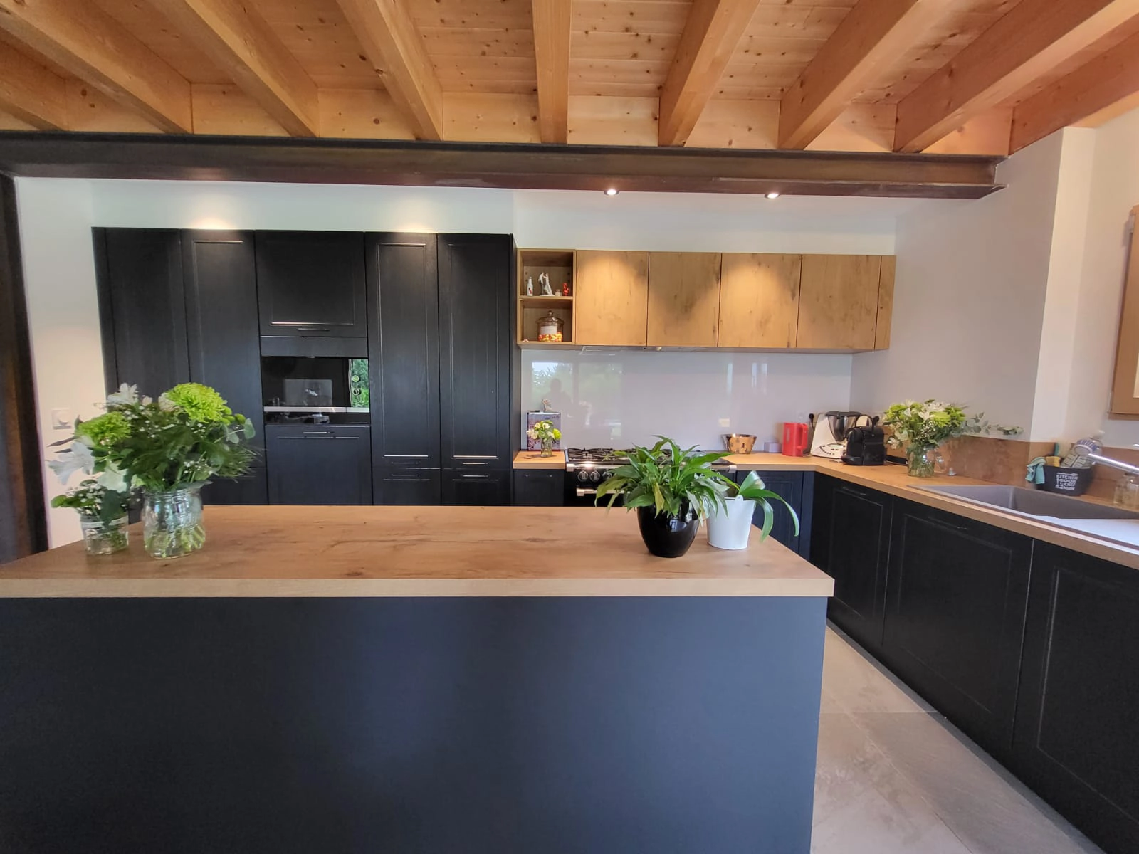 Vue d'ensemble d'une cuisine architecturale noire et bois avec un grand îlot central servant de point d'ancrage et de lieu de partage dans la pièce de vie.