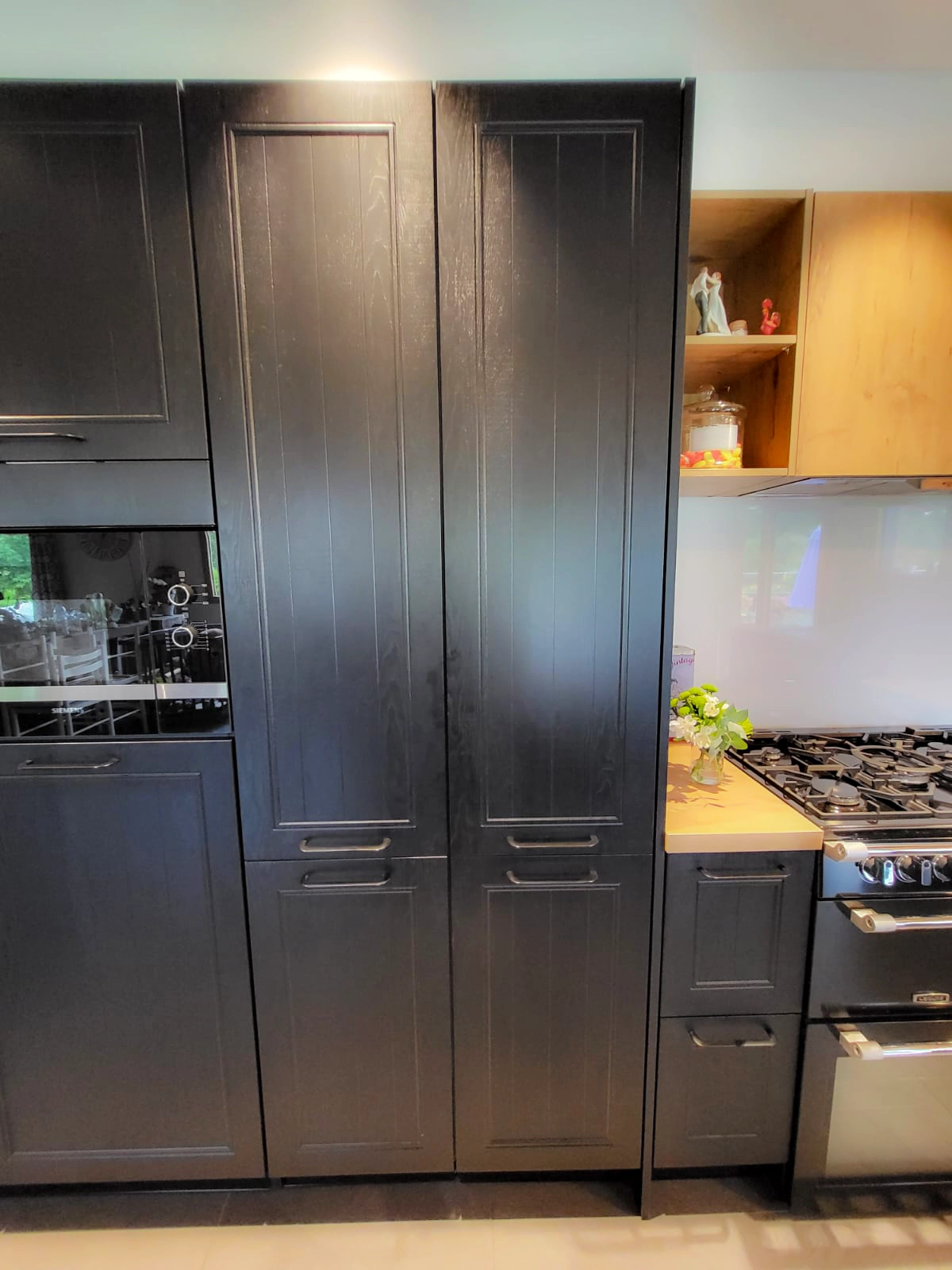 Mur de colonnes de cuisine aux façades sombres et élégantes avec électroménager intégré et une porte secrète parfaitement dissimulée dans l'alignement du mobilier.