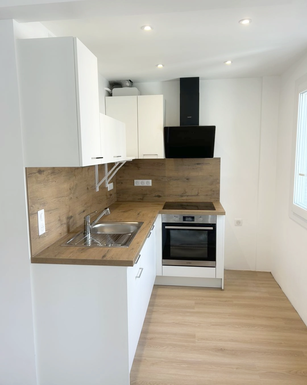 Petite cuisine en L blanche avec plan de travail bois, aménagement optimisé pour maximiser les rangements dans un espace réduit