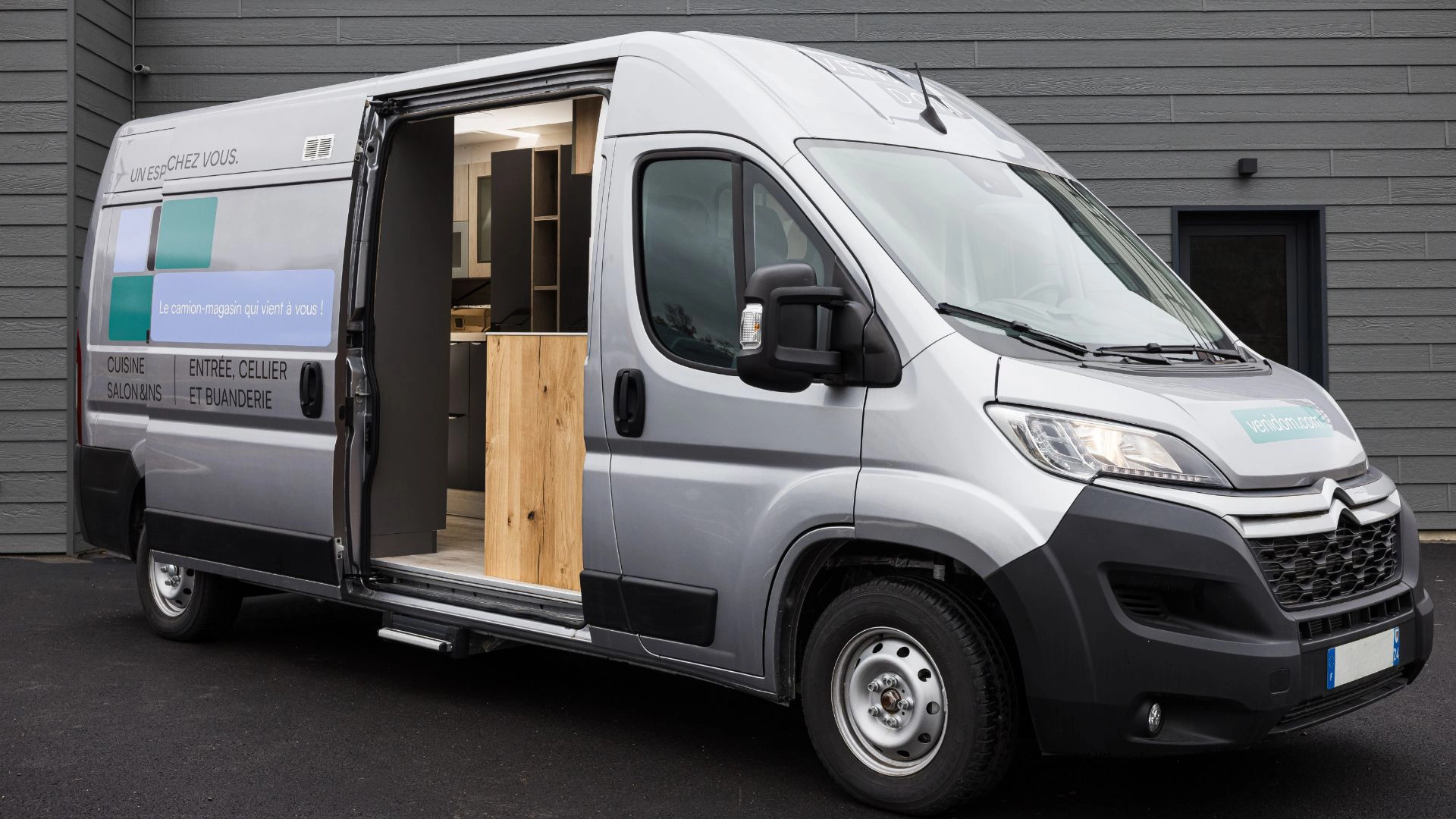 Camion-magasin gris de la marque Venidom vu de trois-quarts avant avec la porte latérale ouverte, présentant des échantillons d'aménagement intérieur.