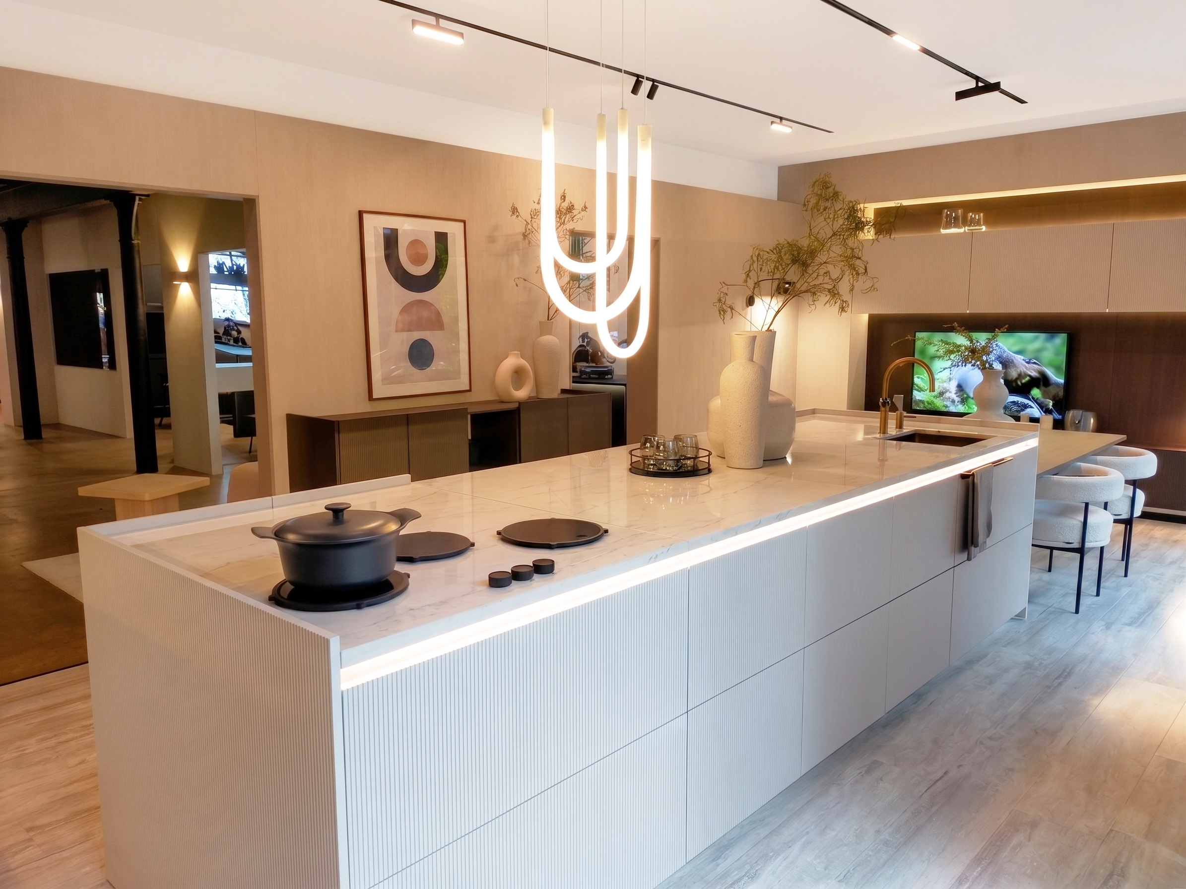 Vue d'ensemble d'une cuisine design et épurée avec un très long îlot central en marbre blanc, un luminaire suspendu néon original et des tabourets de bar blancs.