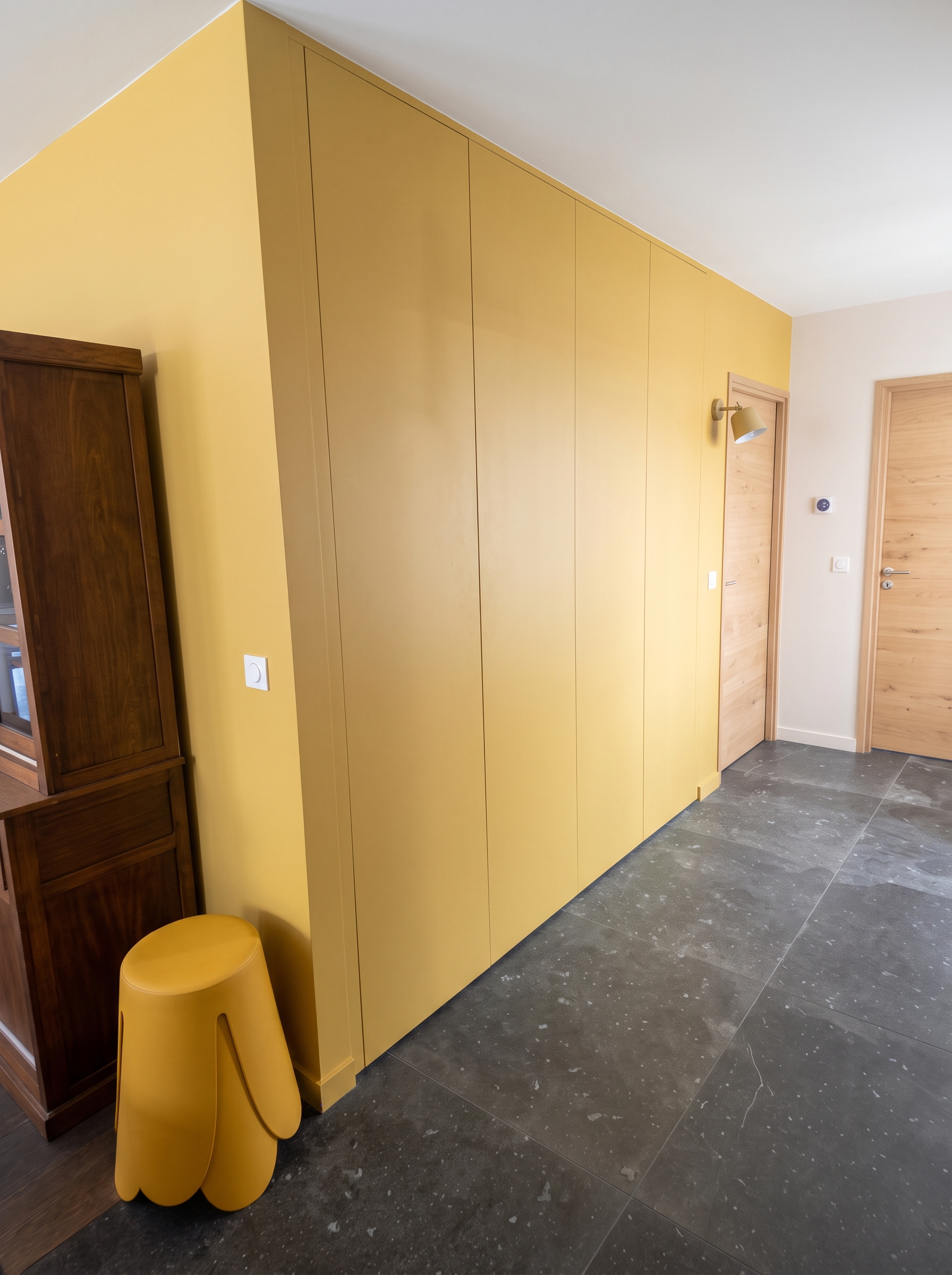 Entrée chaleureuse aux tons jaune miel avec portes sans poignées et rangements optimisés.